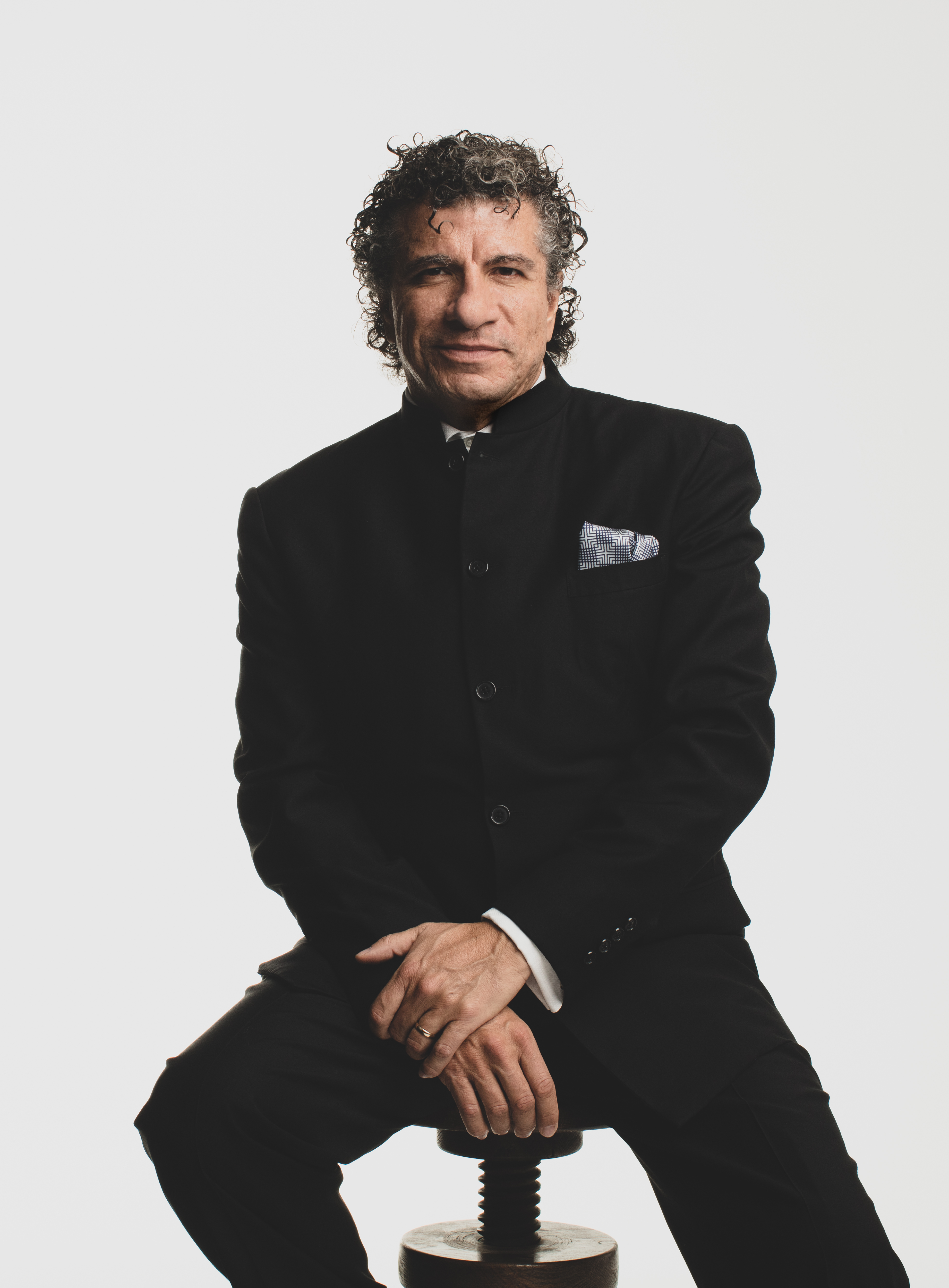 Giancarlo Guerrero sitting on a stool in front of a beige background
