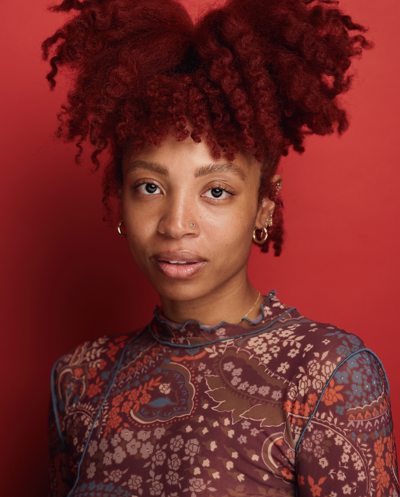 A-Larenée Davis wearing a red top with red highlighted hair, set against a red background