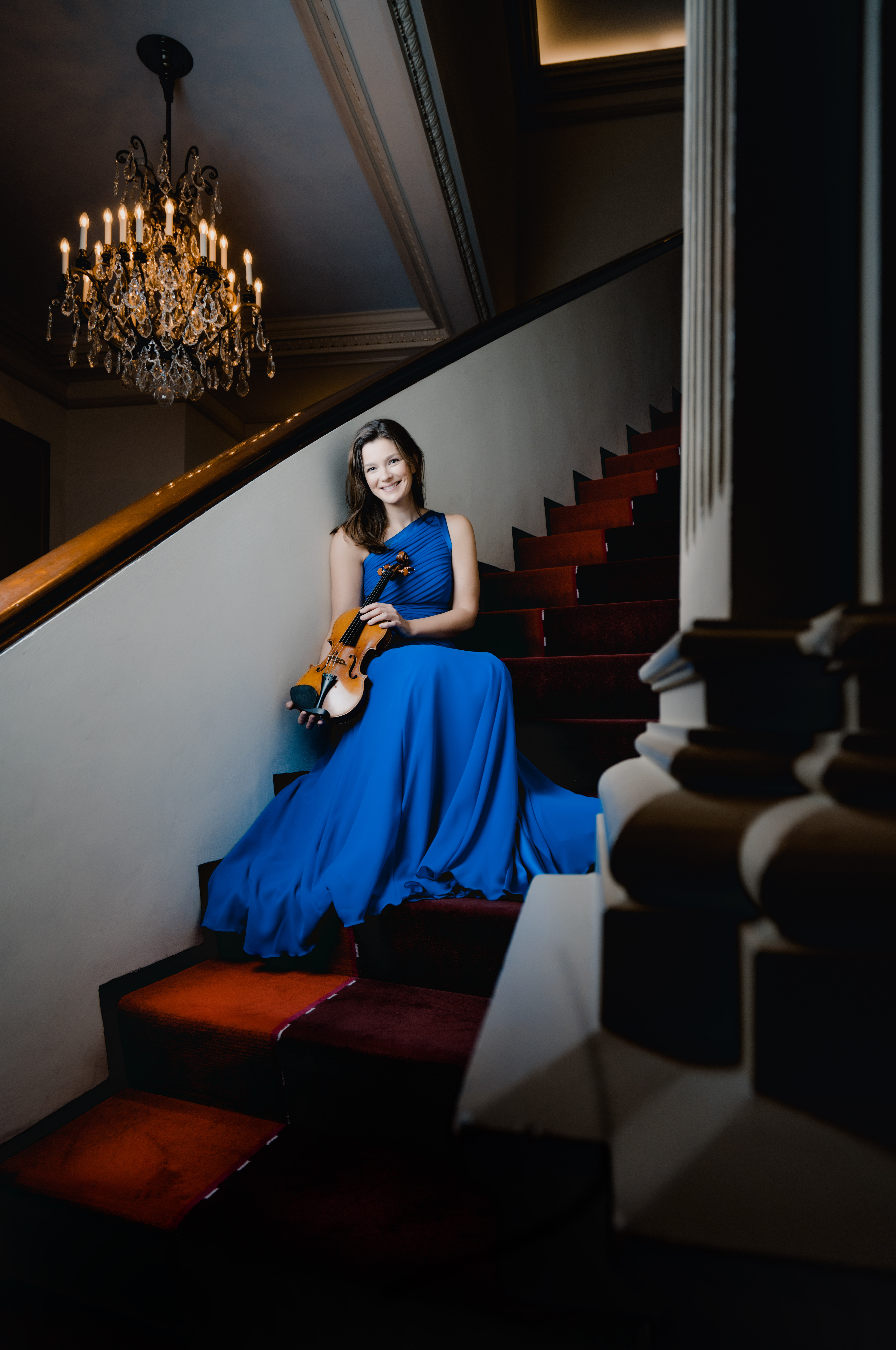 Janine Jansen on a staircase, wearing a blue dress and holding her violin