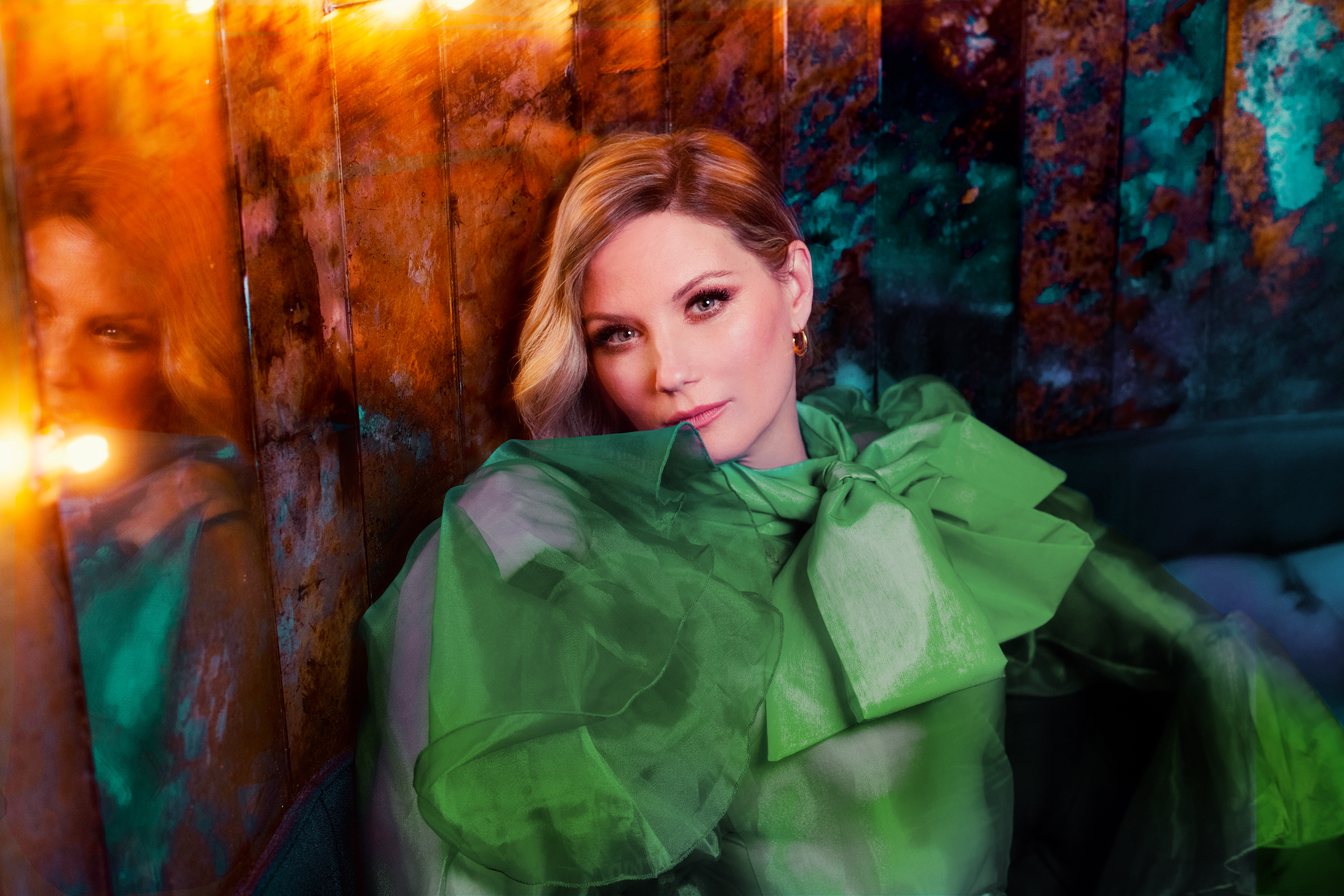 Jennifer Nettles wearing a green jacket, lounging against a multicolored background