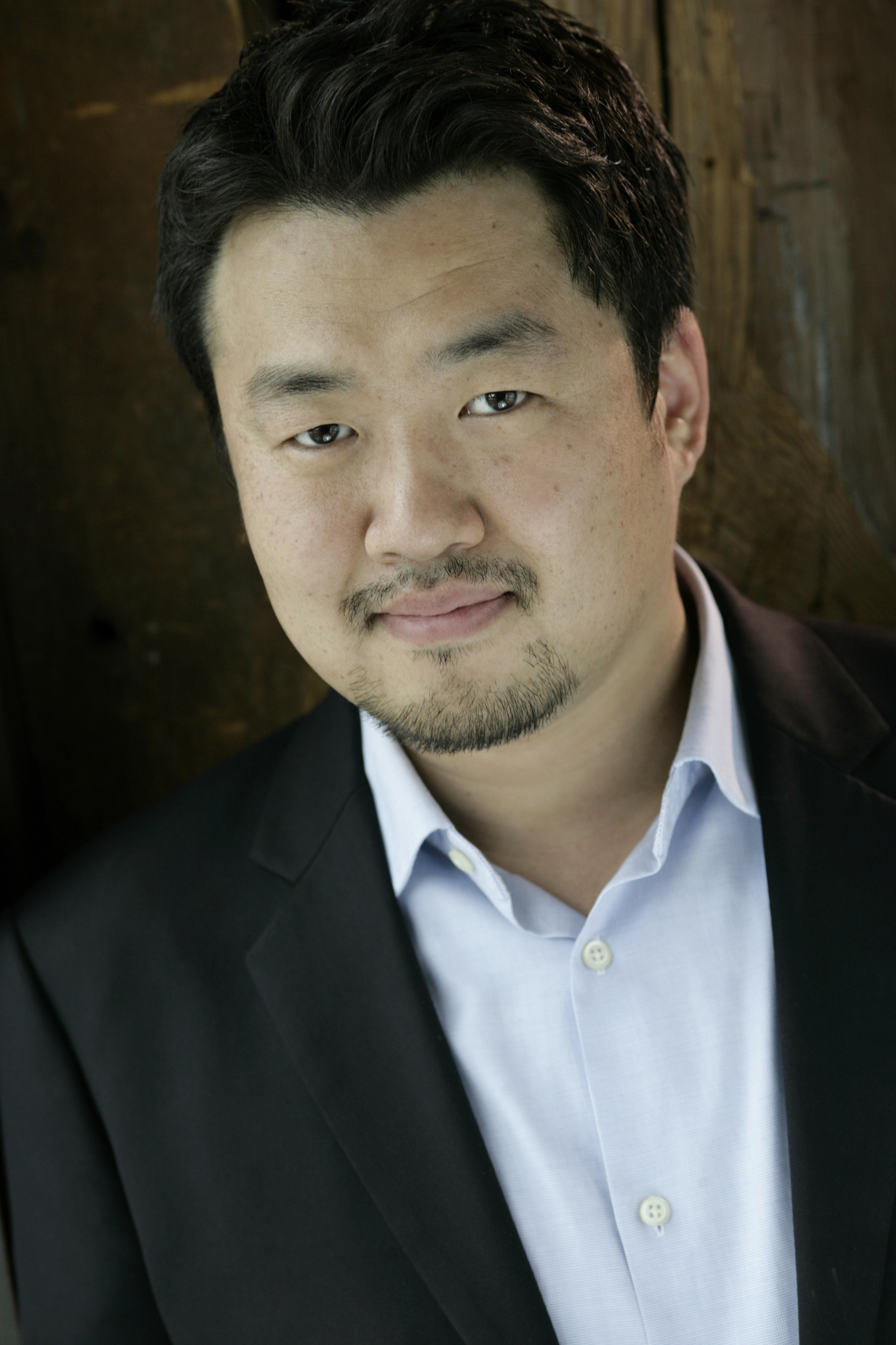 Joo Won Kang looking at the camera, wearing a open collared shirt with a black suit jacket