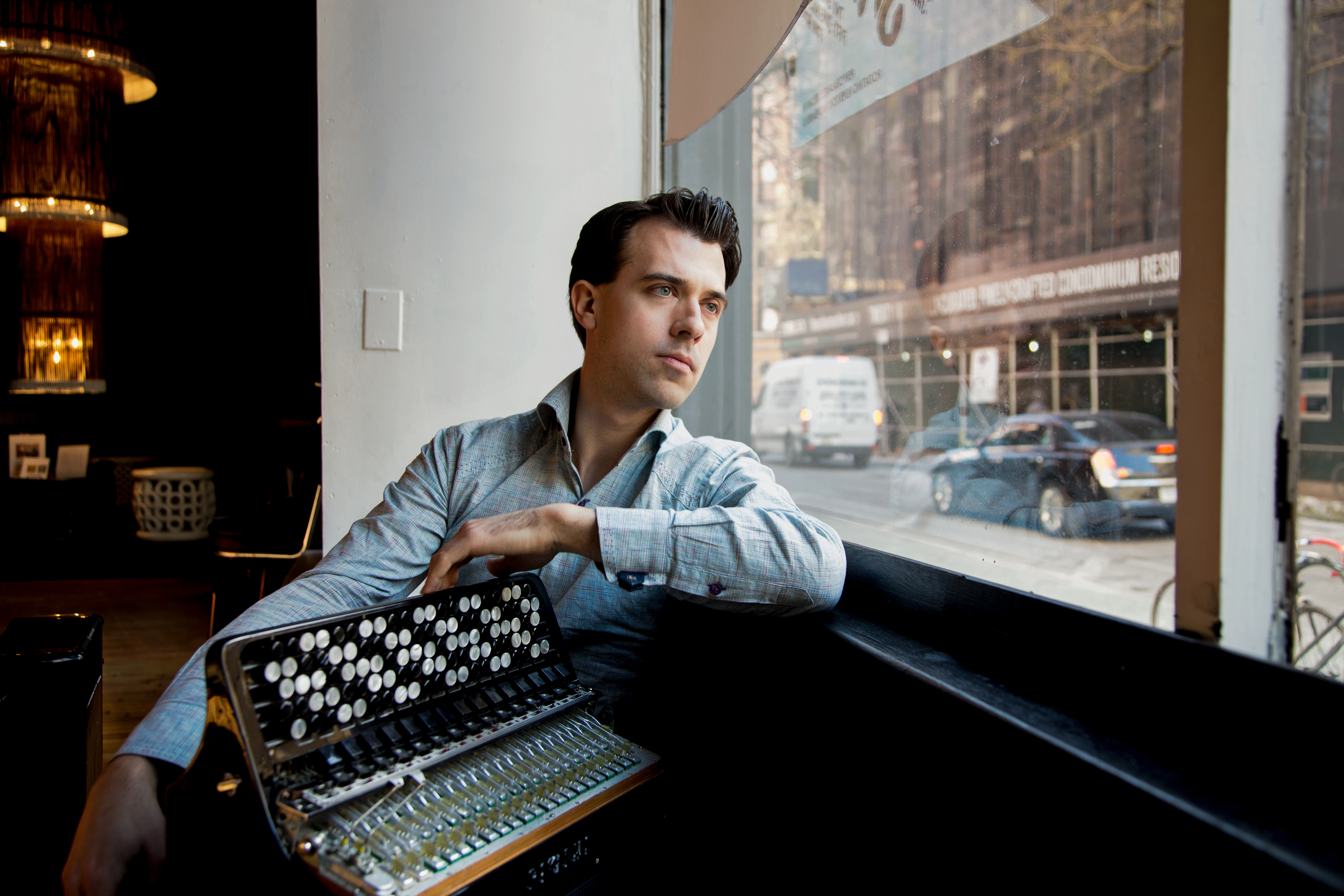 Photo of Julien Labro sitting down with his accordian looking out a window.