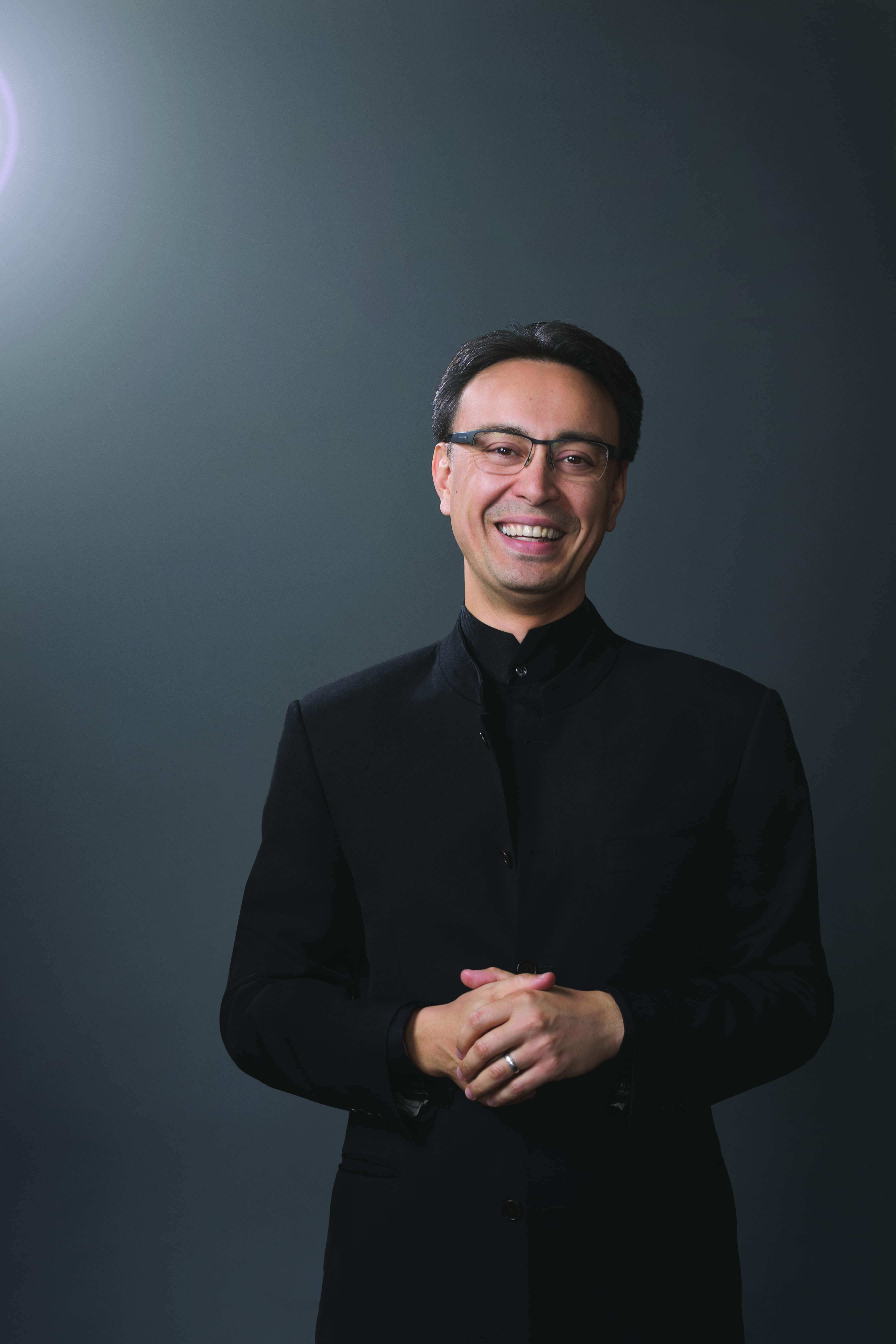 Ken-David Masur smiling while standing in front of a blue background