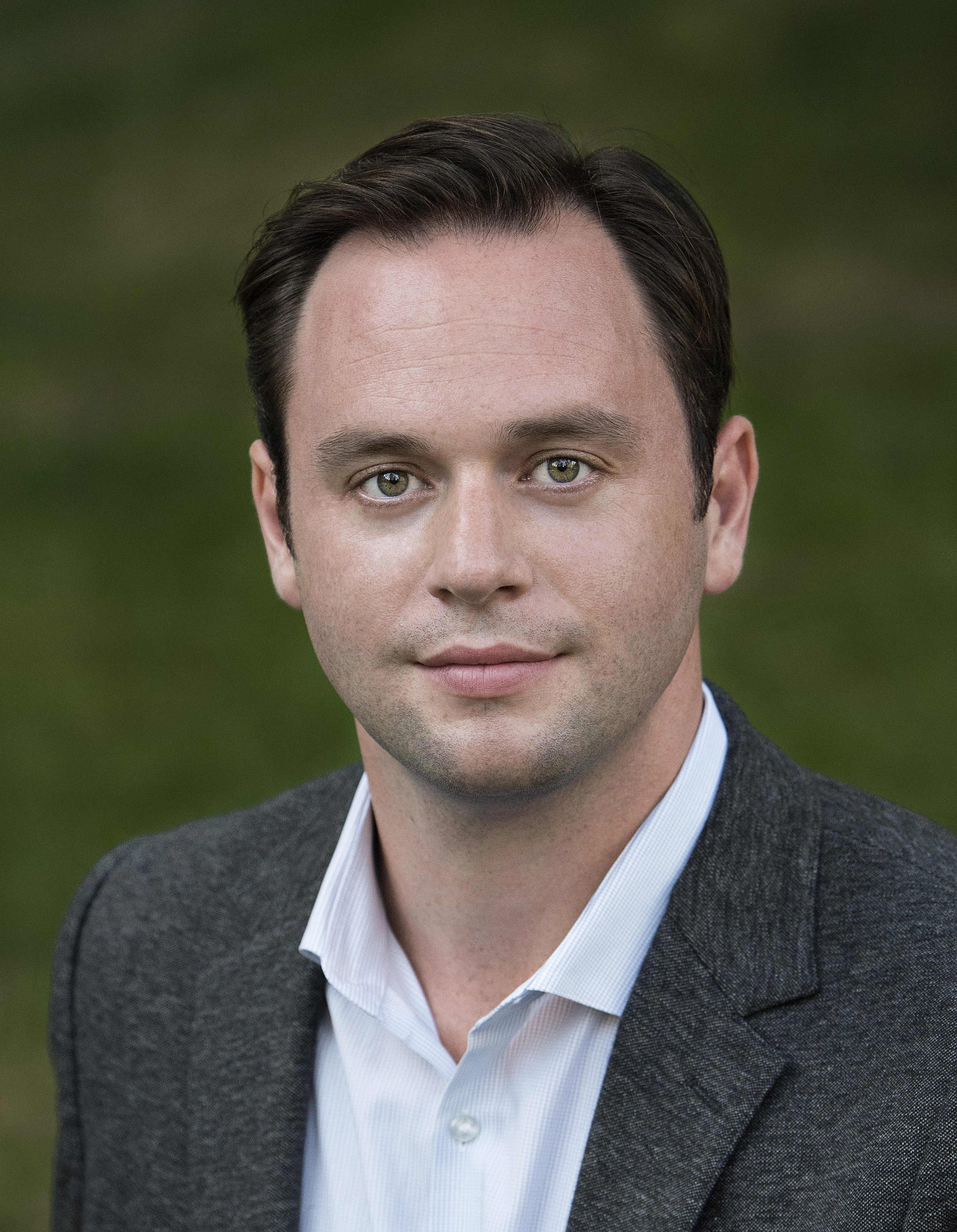 Headshot of Paul Appleby wearing a suit with grass in the background