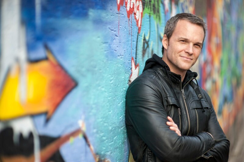 Headshot of Ryan McKinny standing with his arms crossed and leaning against a colorful wall
