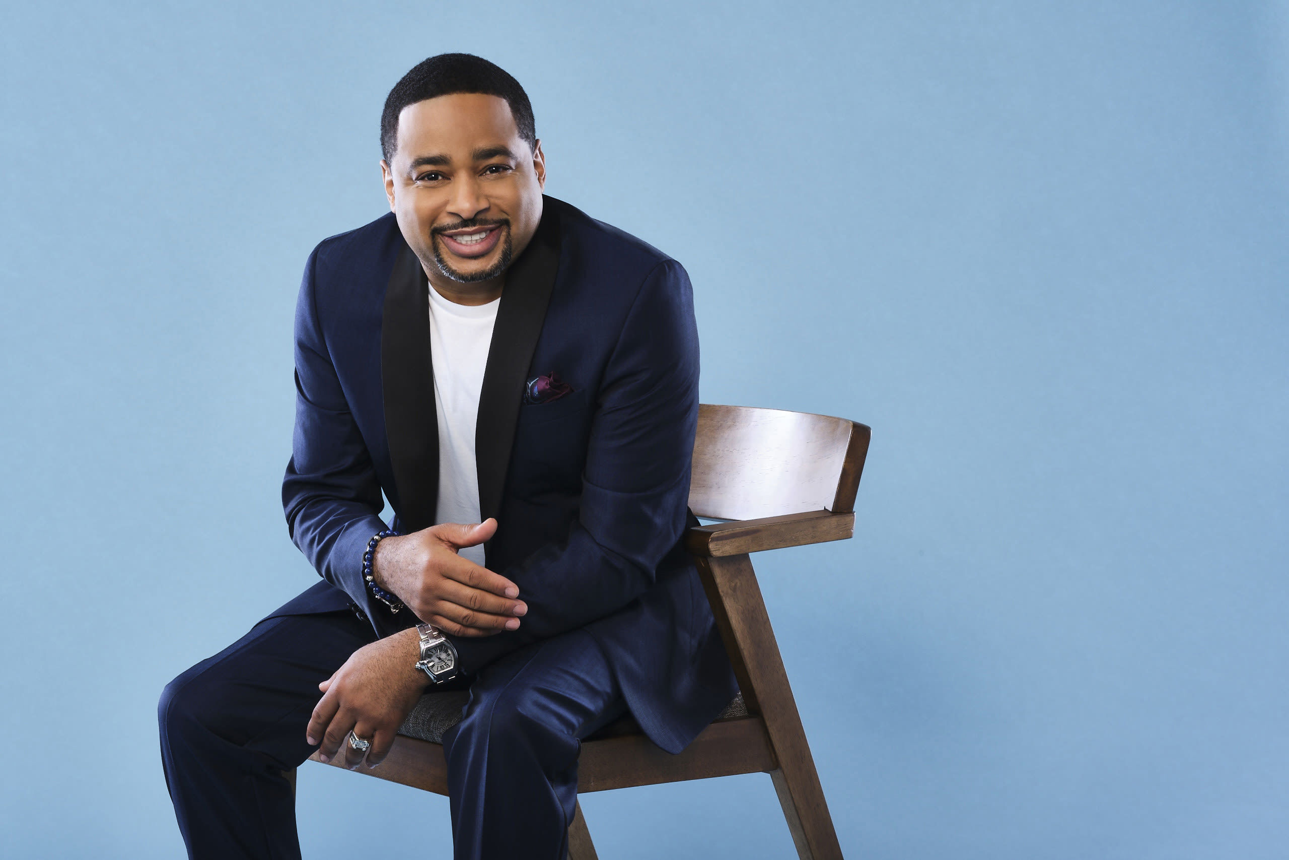 Smokie Norful sitting in a chair wearing a blue suit jacket