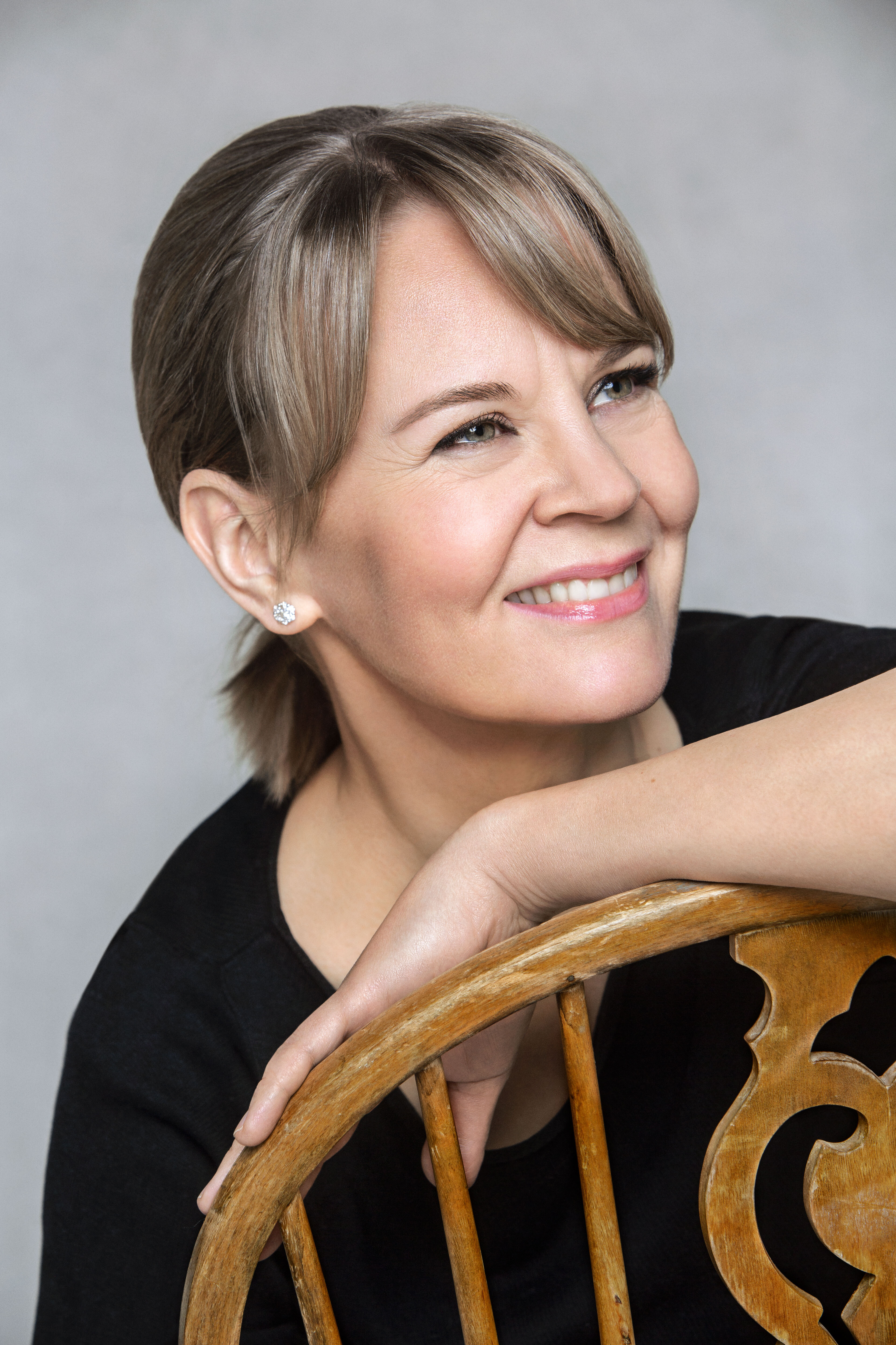 Susanna Mälkki sitting on a wooden chair, smiling