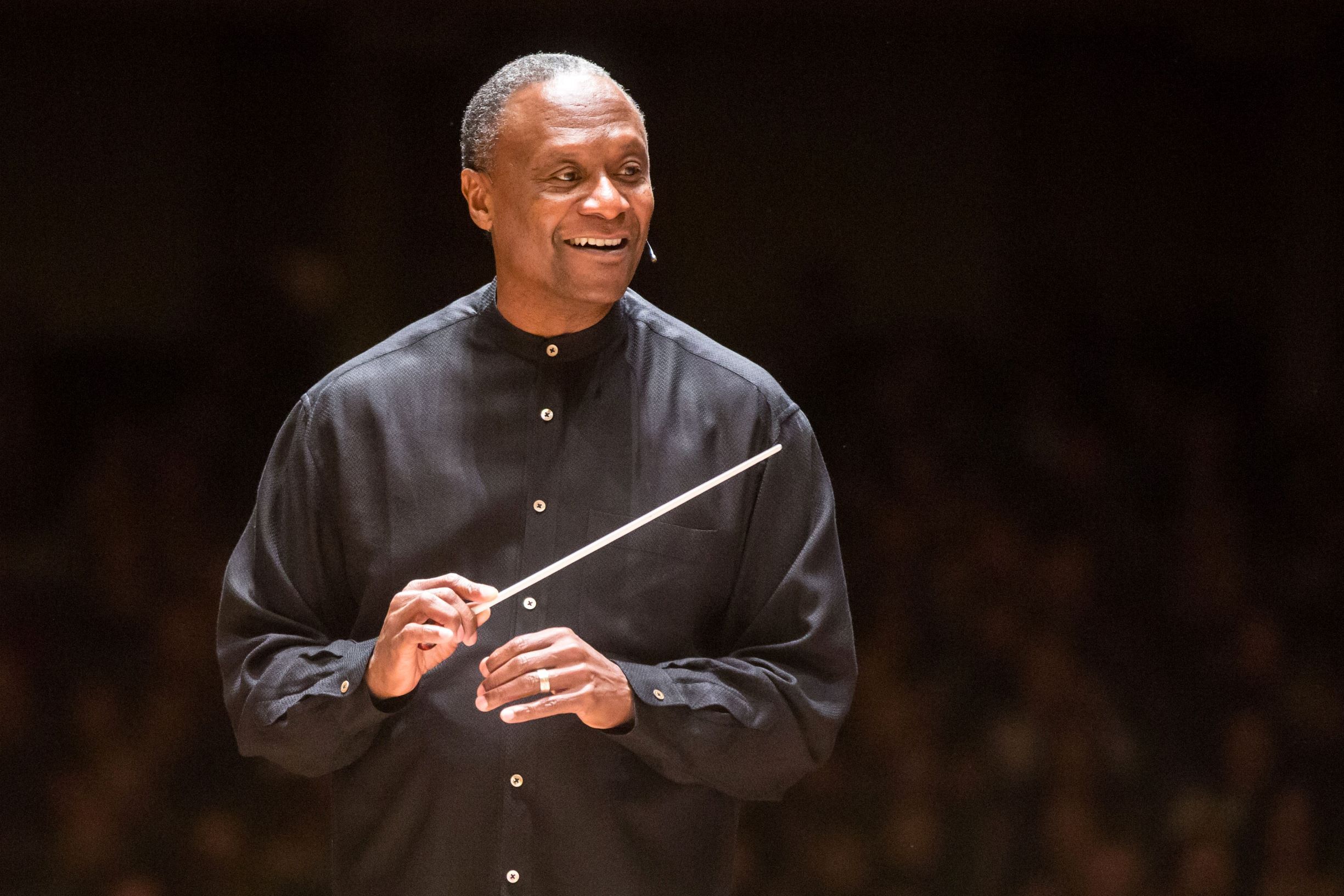 Conductor Thomas Wilkins holding his baton and smiling onstage.