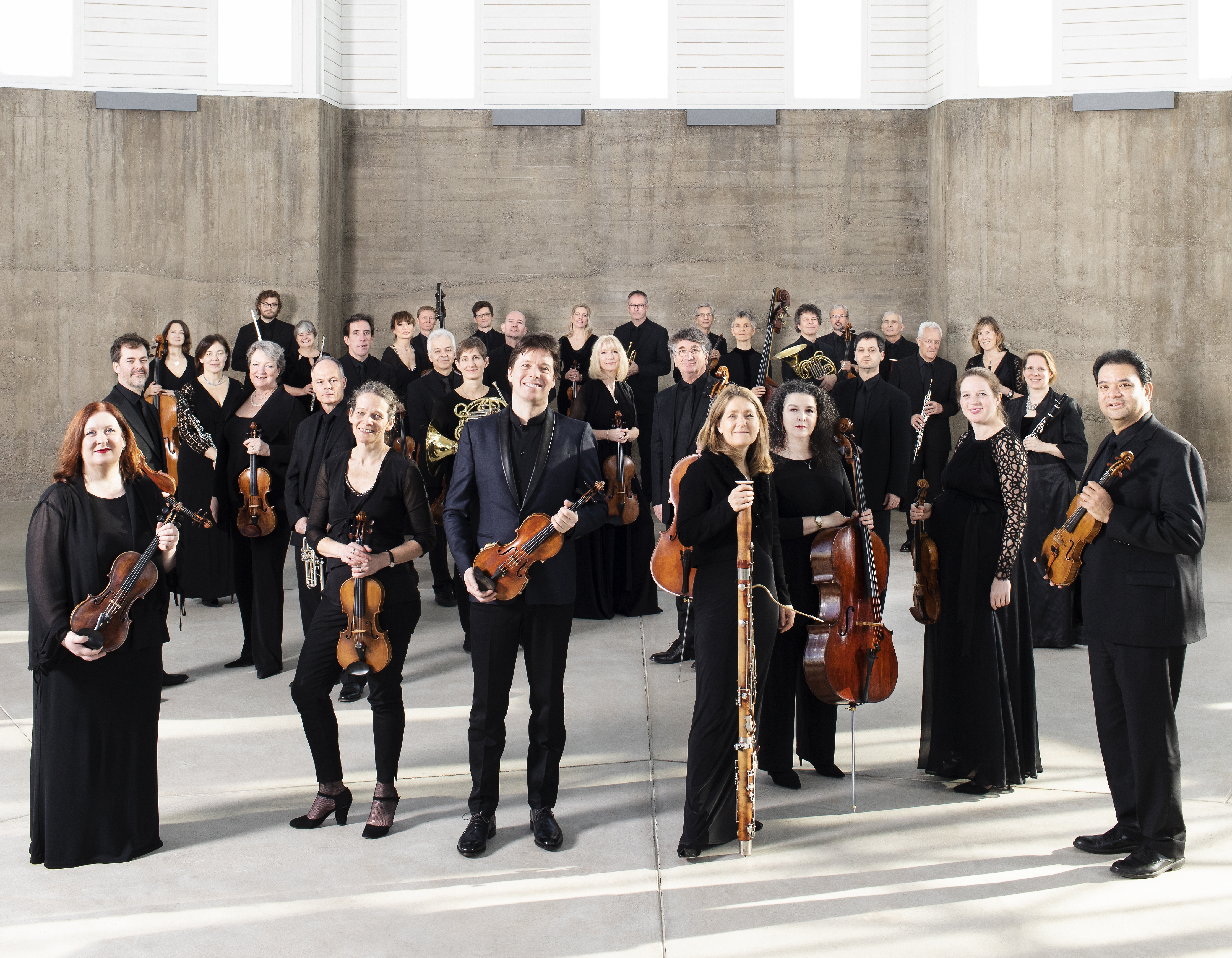 Academy of St Martin ensemble with Joshua Bell, standing in front of a beige background