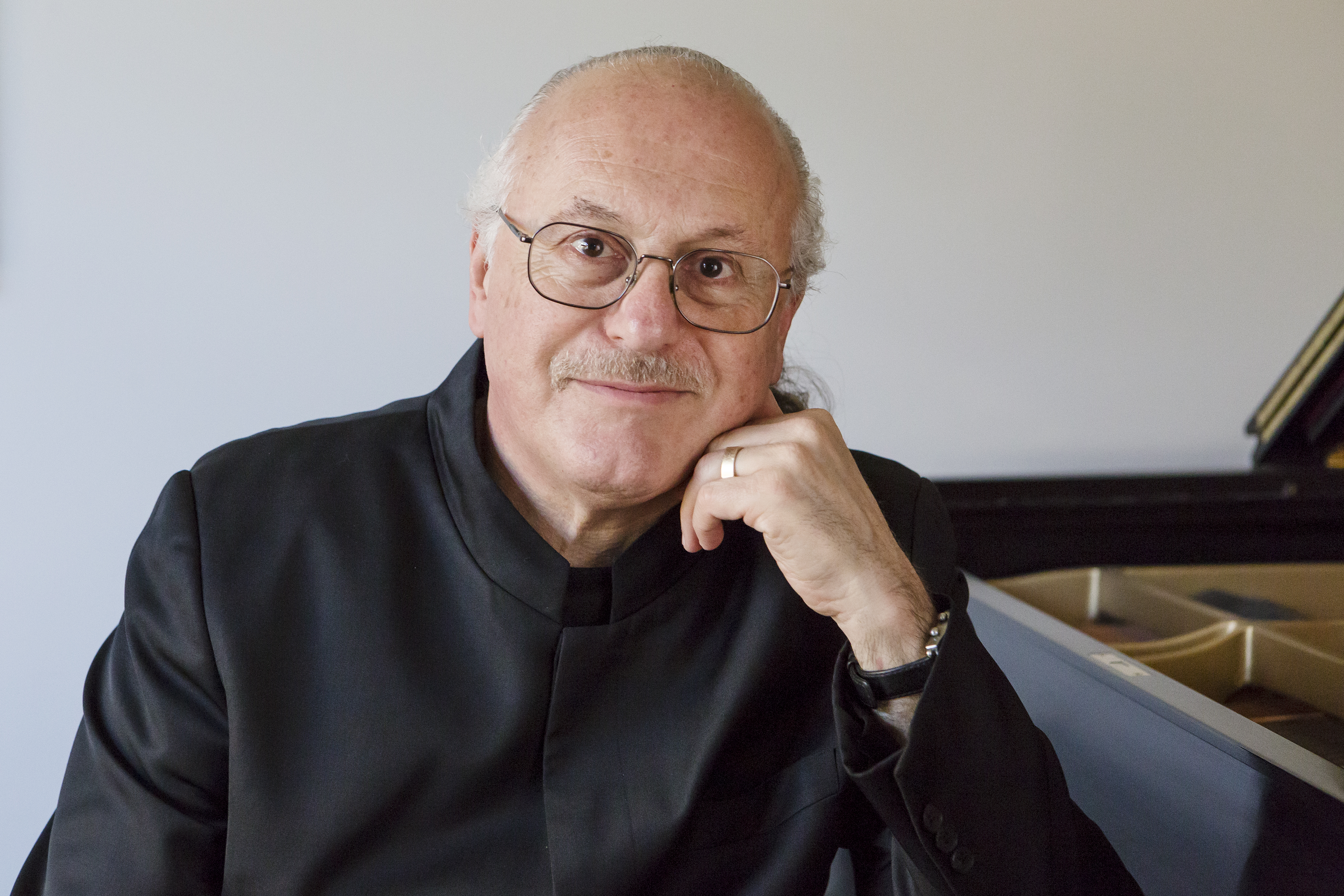 Arnie Roth sitting in front of a piano with his left hand resting on his chin