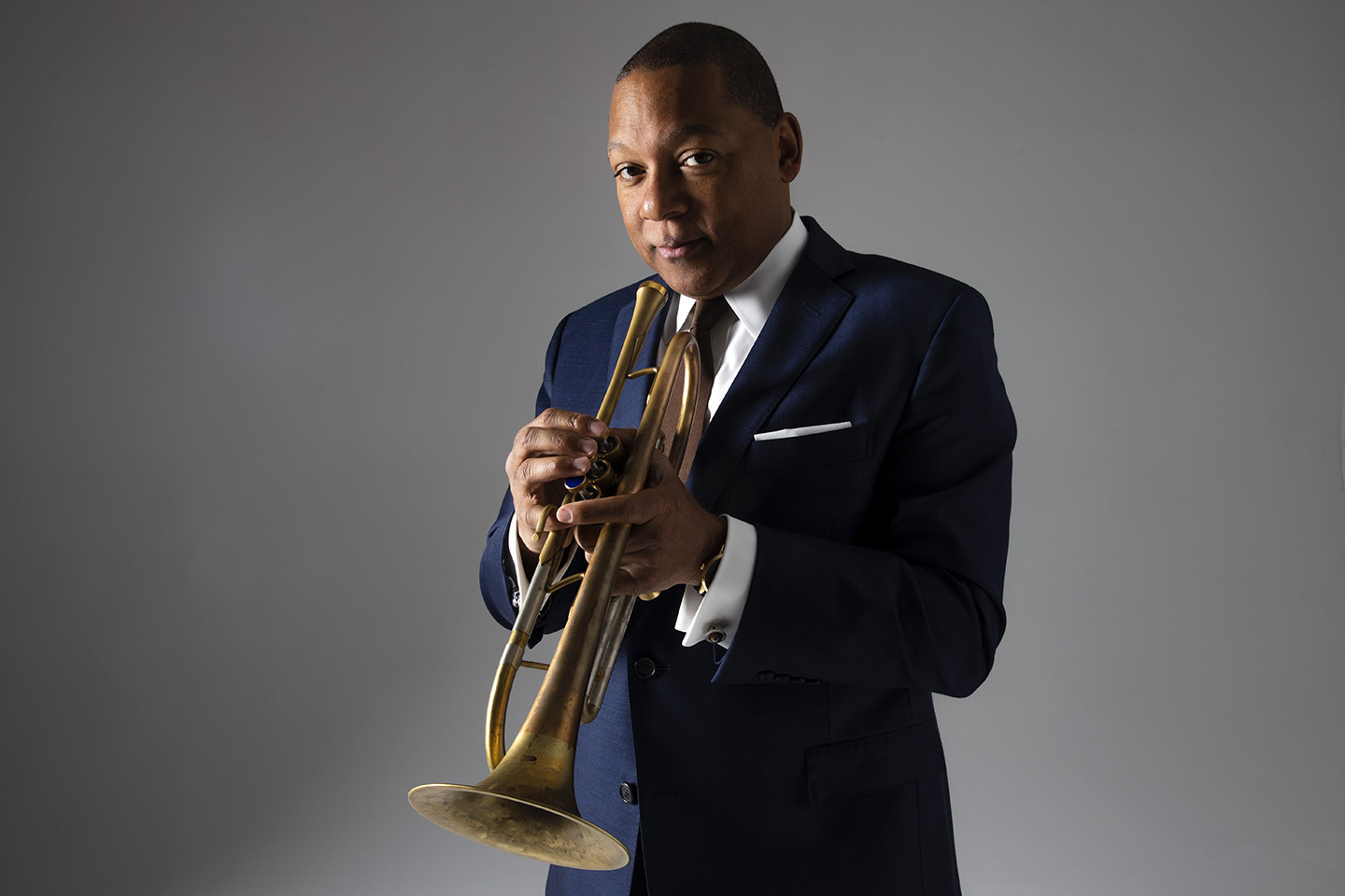 Wynton Marsalis holding a trumpet in front of a grey background