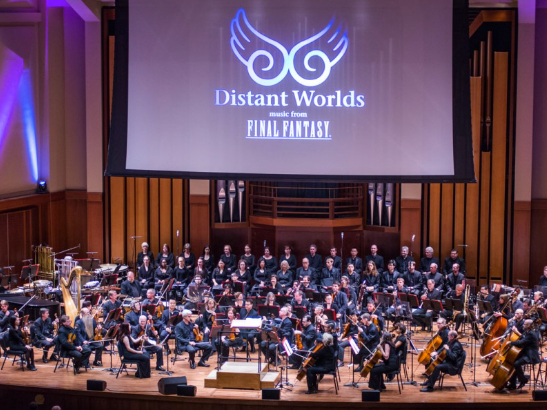 an orchestra and chorus on stage in front of a large screen with the word "distant words: music from Final Fantasy" showing