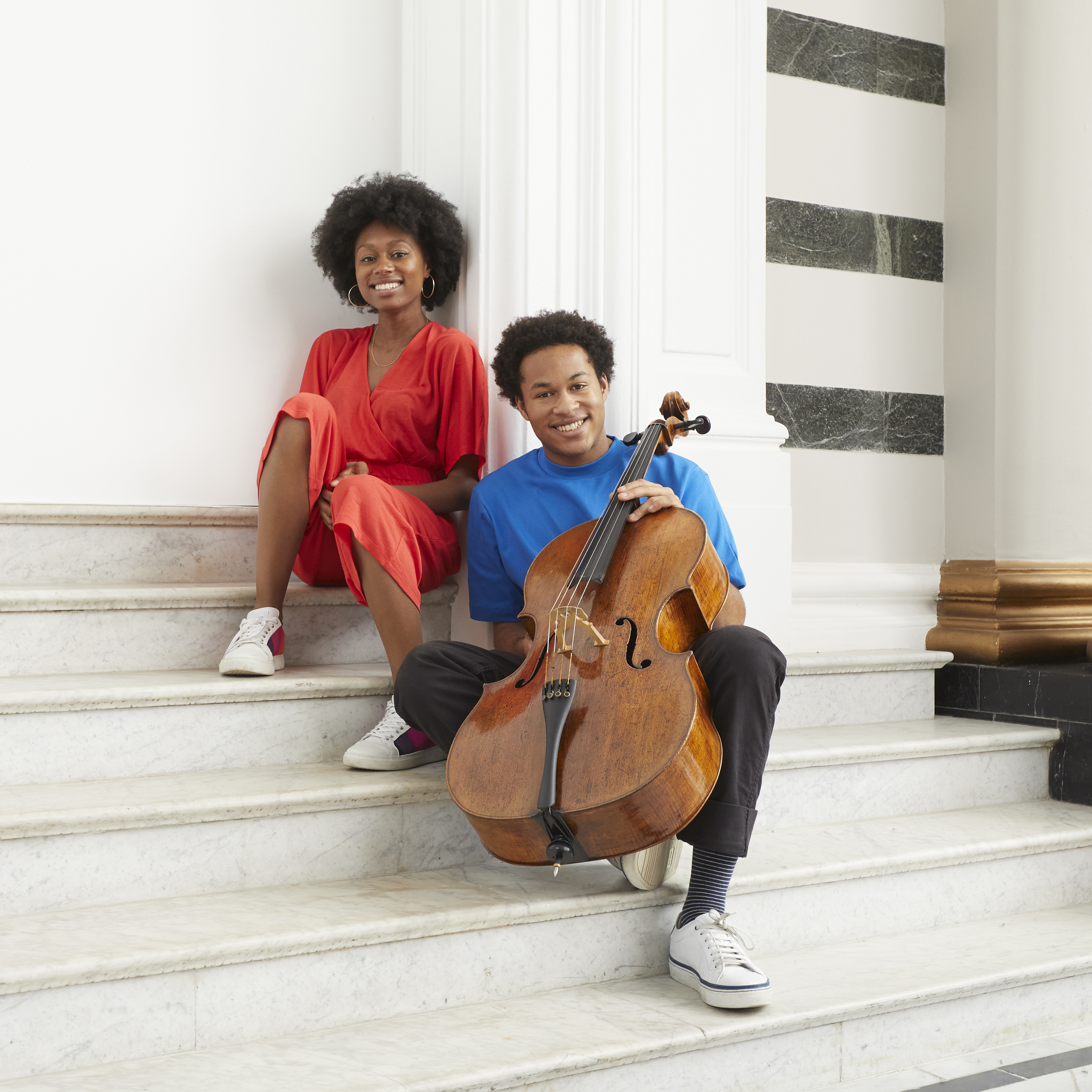 Sheku Kanneh-Mason and Isata Kanneh-Mason sitting on a set of white stairs, smiling