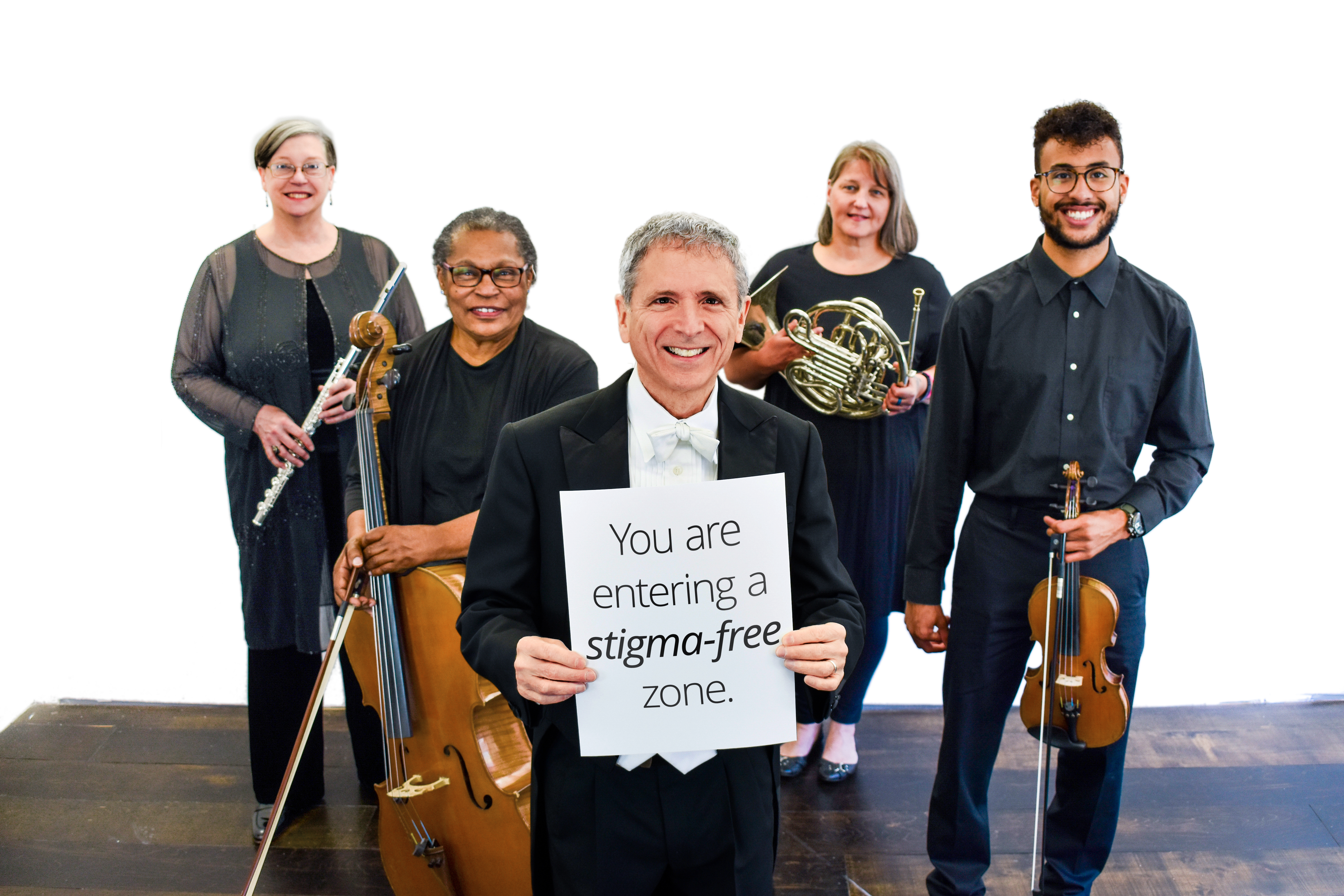 Members of the Me2 Orchestra gathered around a man in the middle who is holding a sign that reads "You are in a stigma-free zone."
