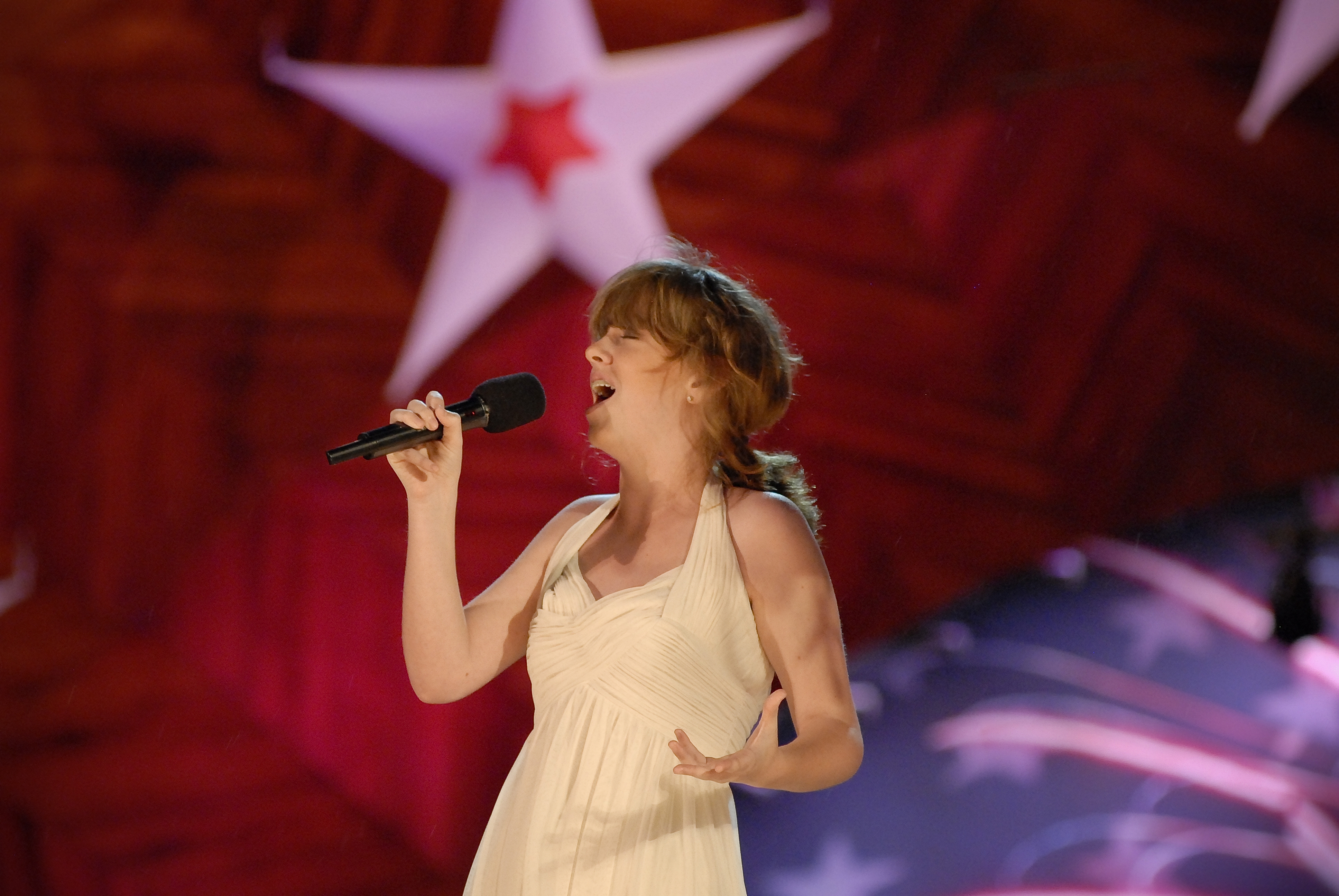 A young woman in a white dress sings on stage