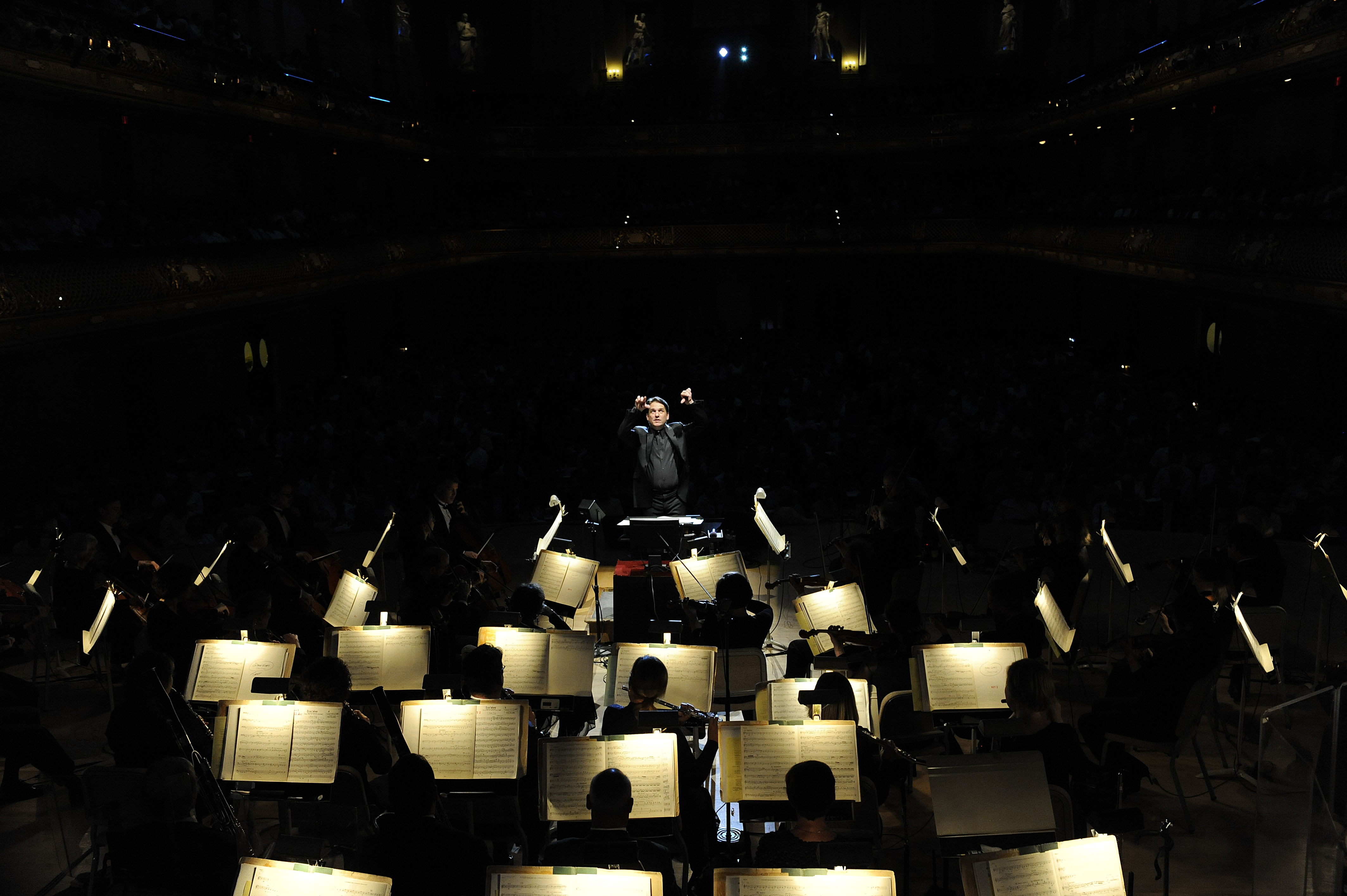 In a dark Symphony Hall, the Boston Pops musicians' stand lights glow and Keith Lockhart conducts the players