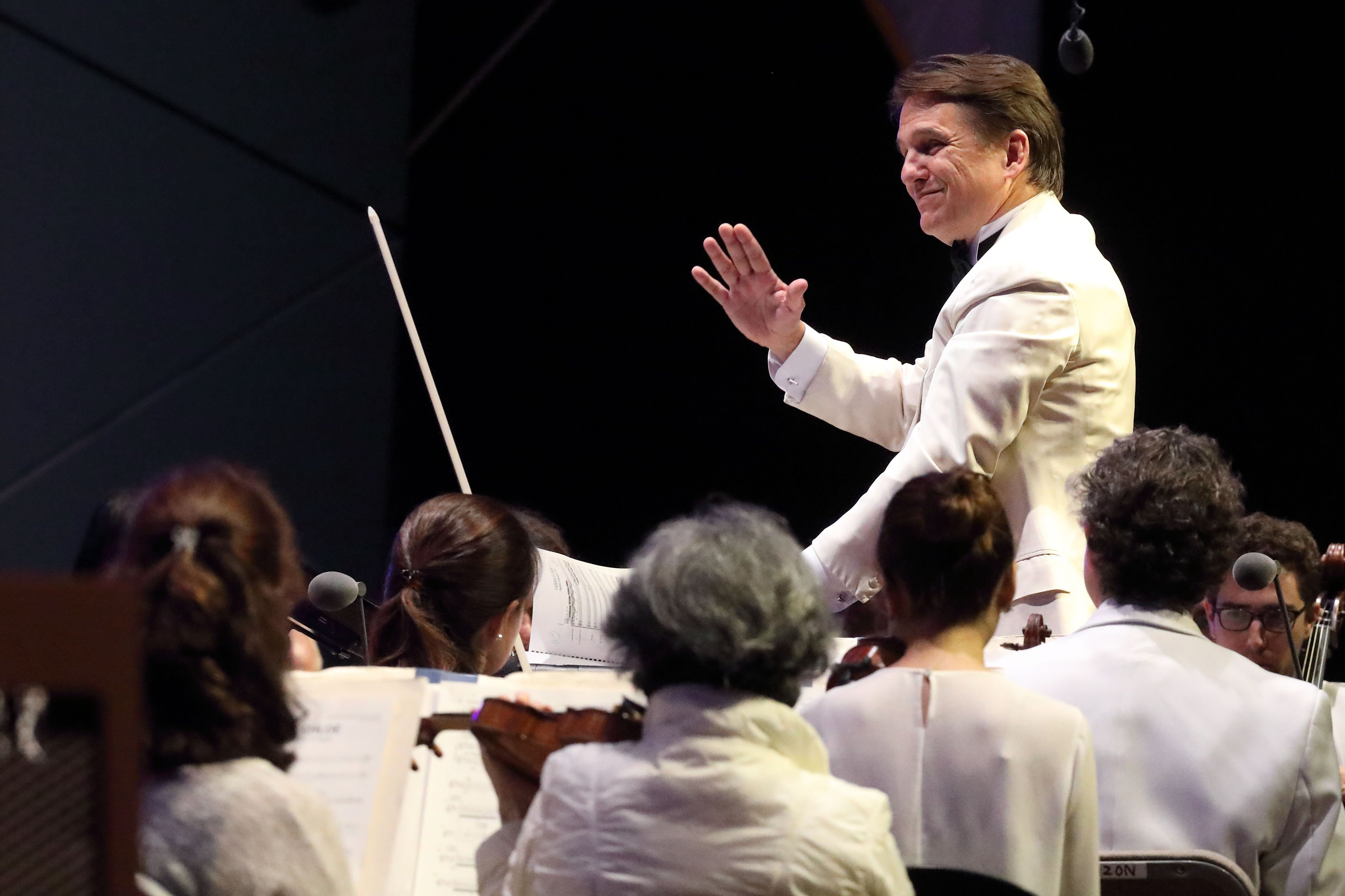 Keith Lockhart wears a white suit jacket and smiles while conducting the Boston Pops