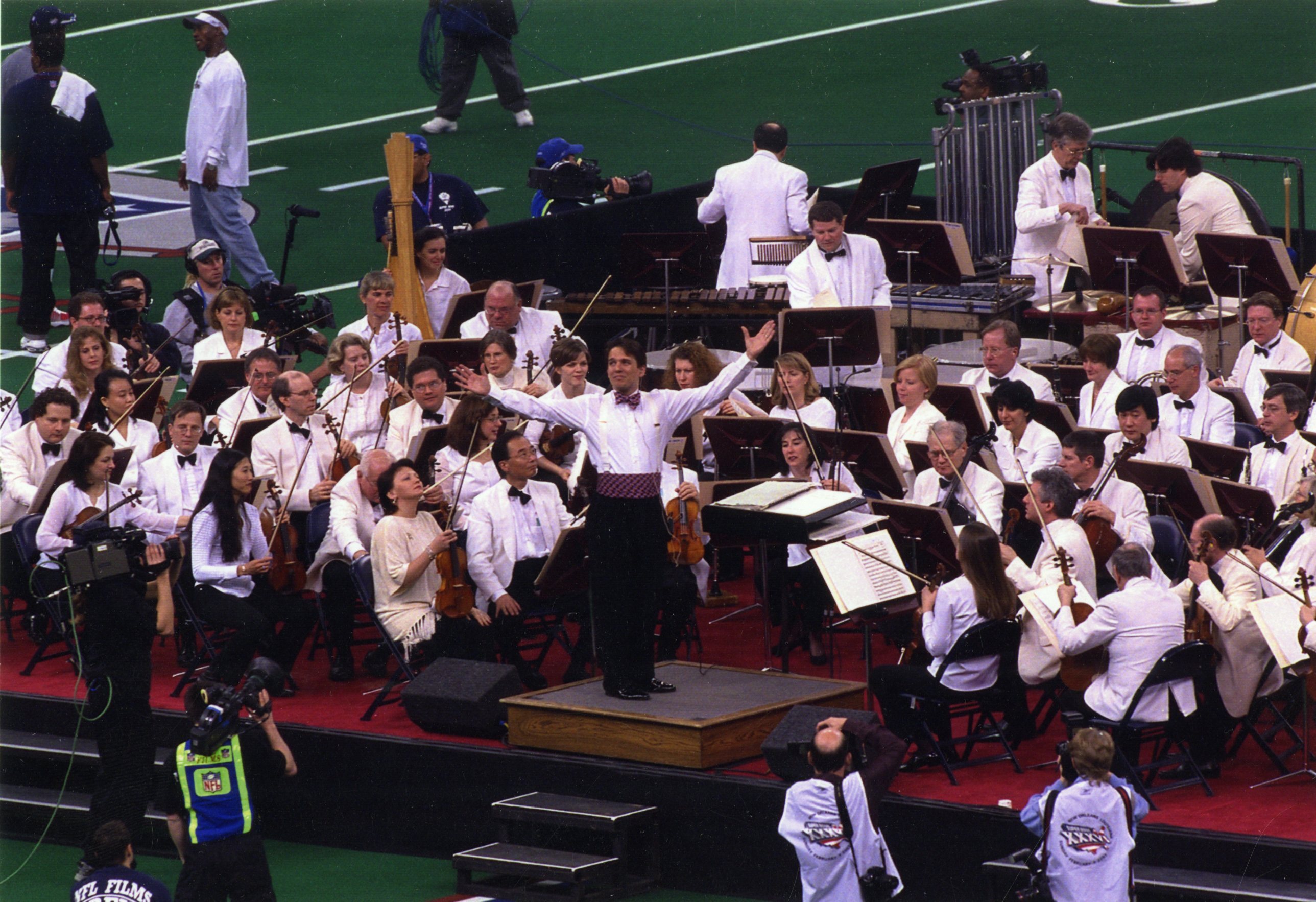 Keith Lockhart and the Boston Pops are dressed in all white on a stage on a football field