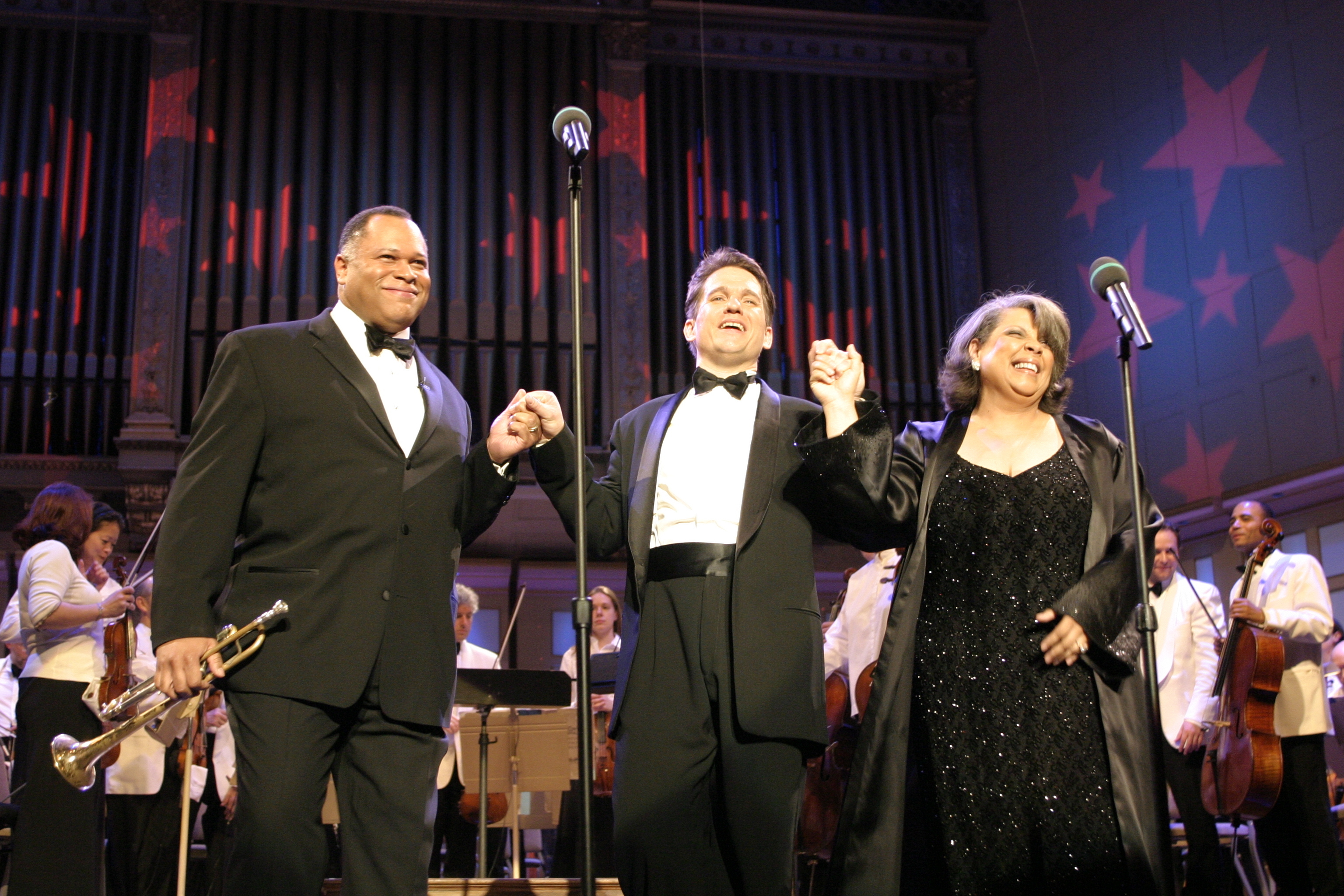 Keith Lockhart stands in center clasping hands with Byron Stripling (holding trumpet) on left and Patti Austin on right