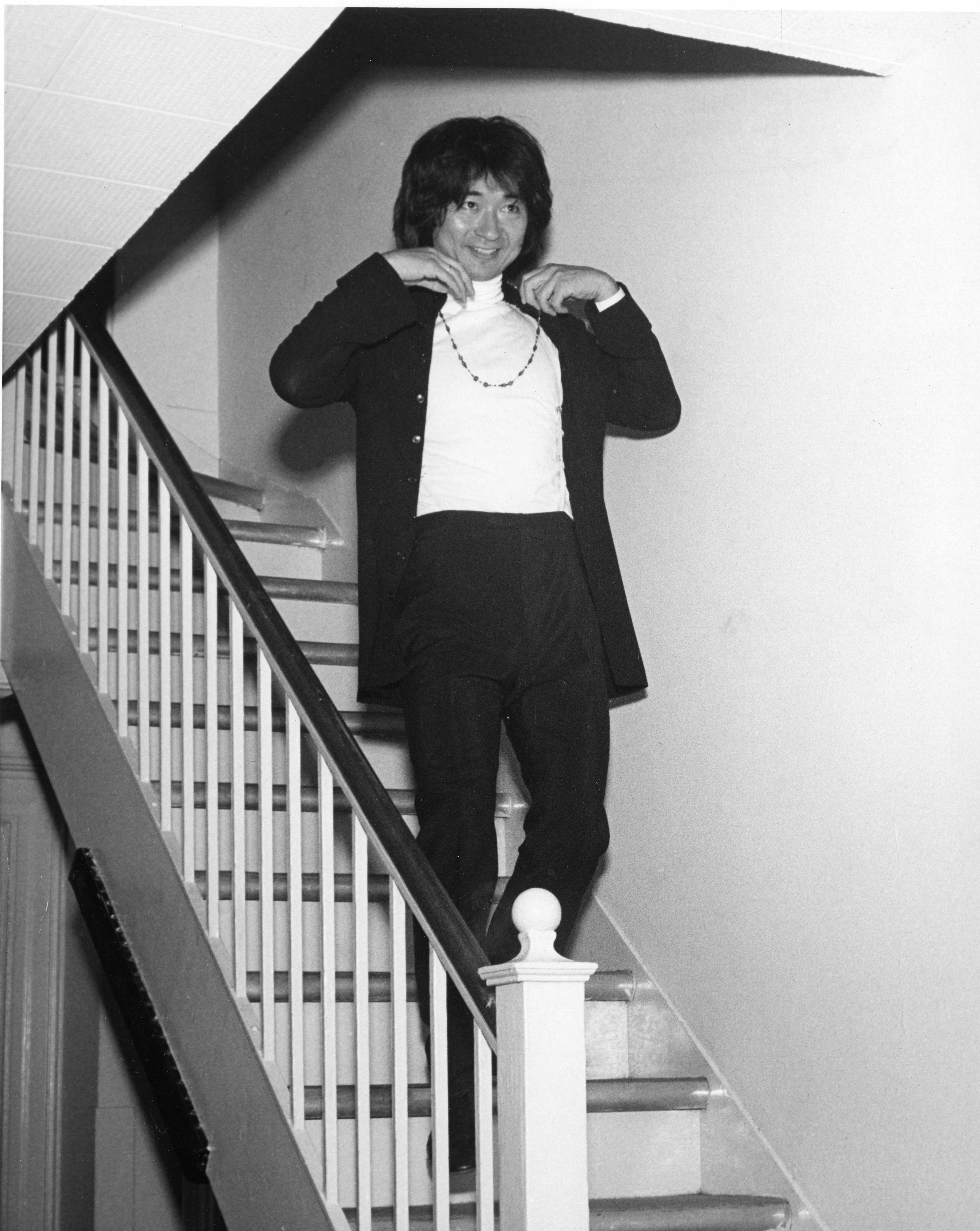 Seiji Ozawa descends the stairs backstage at Symphony Hall wearing his signature beads, 1973