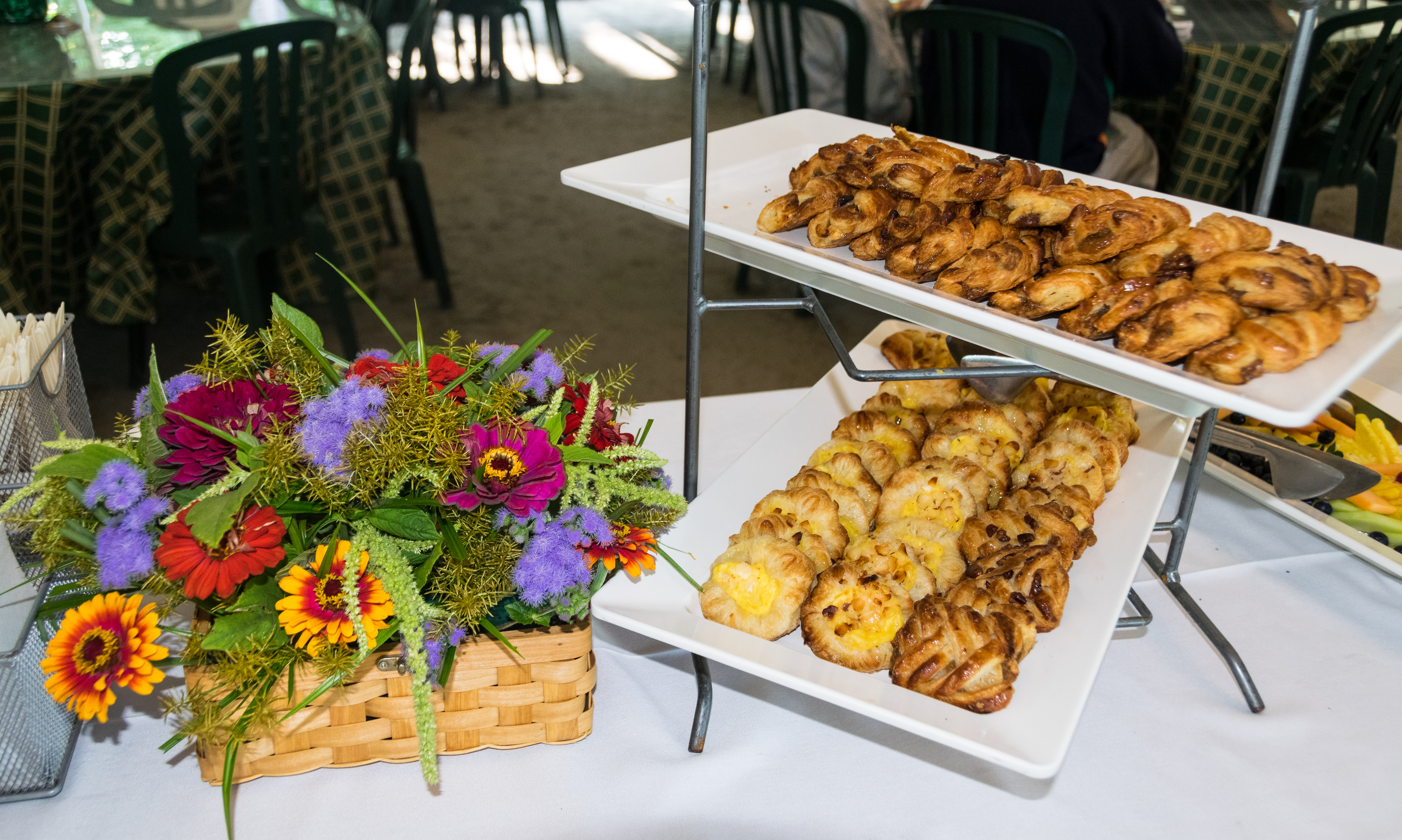 Two white plates with breakfast pastries sits on a table beside a colorful arrangement of flowers in a tent
