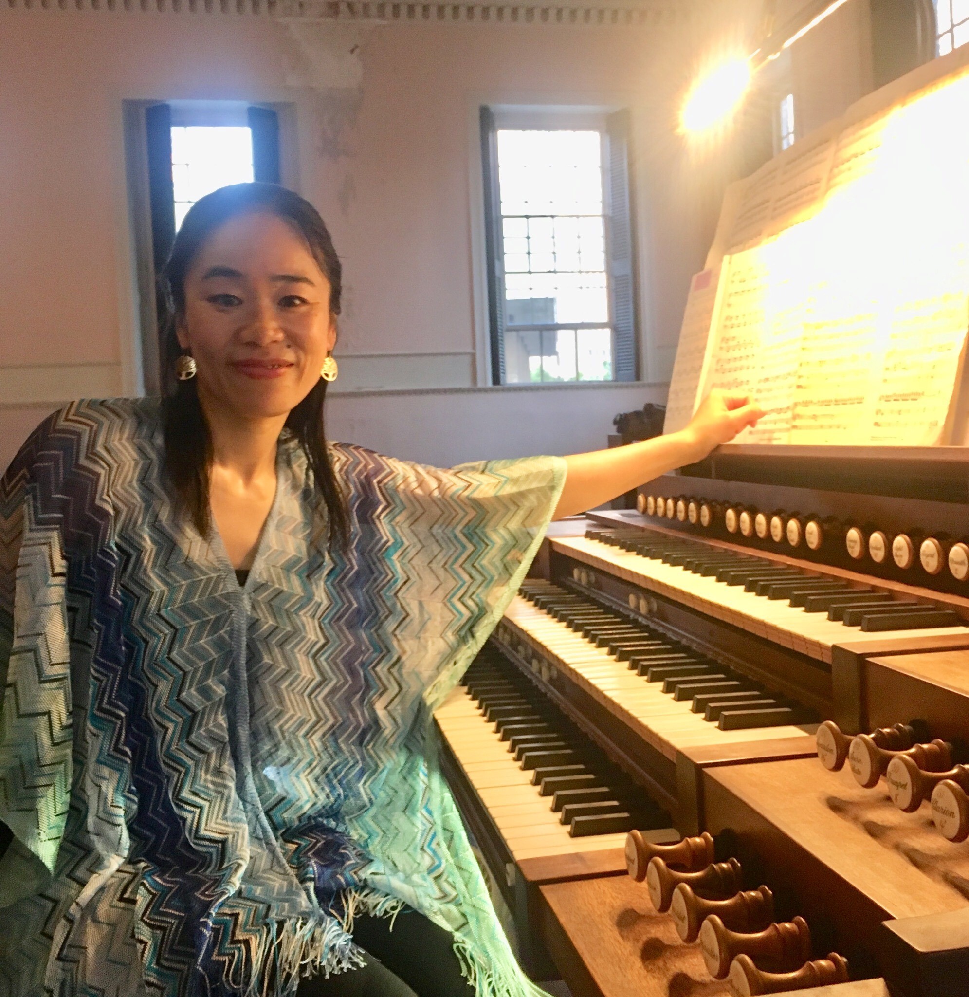 A woman wearing a blue dress sits at a large organ with three sets of keys