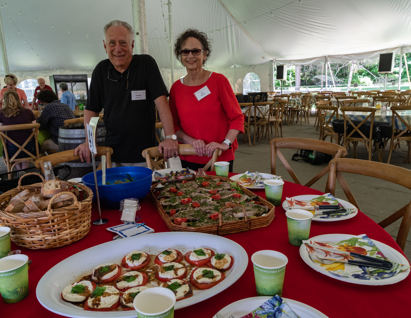 A man in a dark shirt and a woman in a red shirt stand in front of a table filled with food