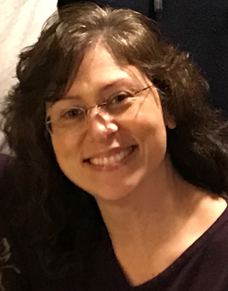 Woman with glasses and brown wavy hair smiling.