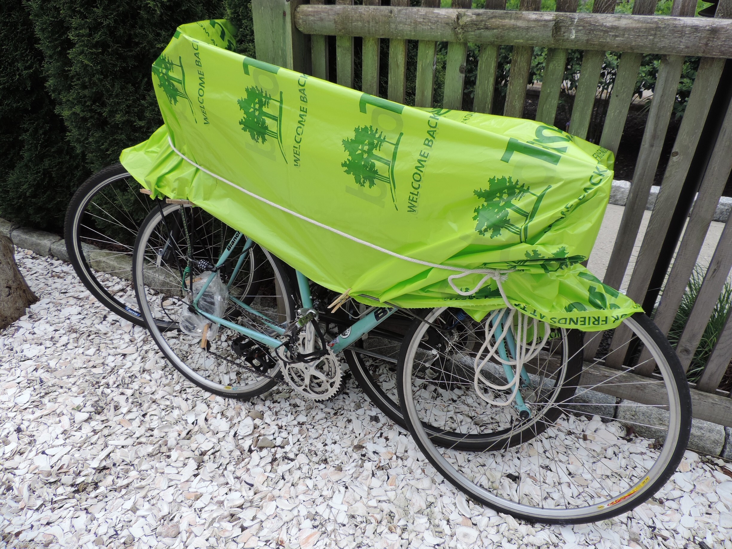 A green tarp covers two bicycles parked against a railing outside