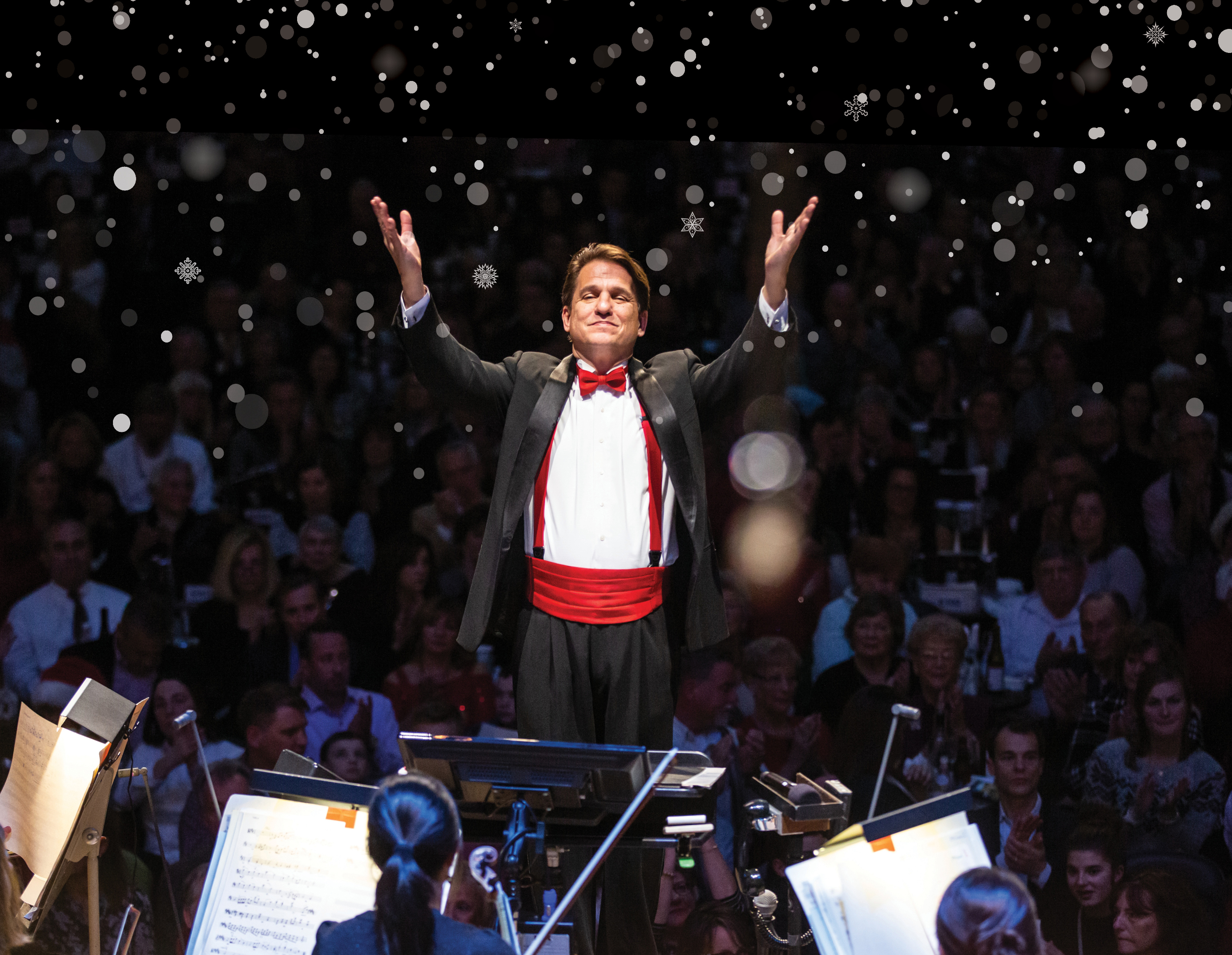 Keith Lockhart conducting with his hands in the air with snow projected behind him.