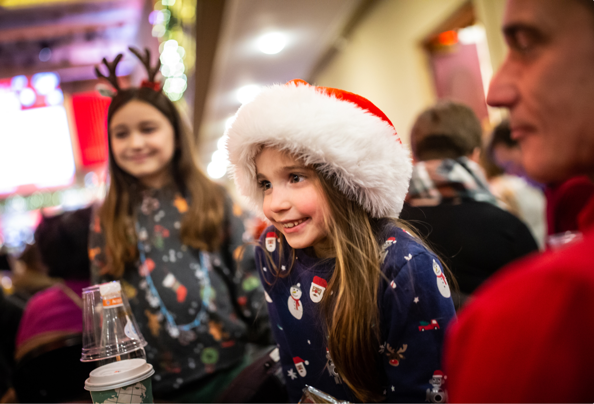 Young girl wearing Sata Claus hat smiles at Holiday Pops concert.