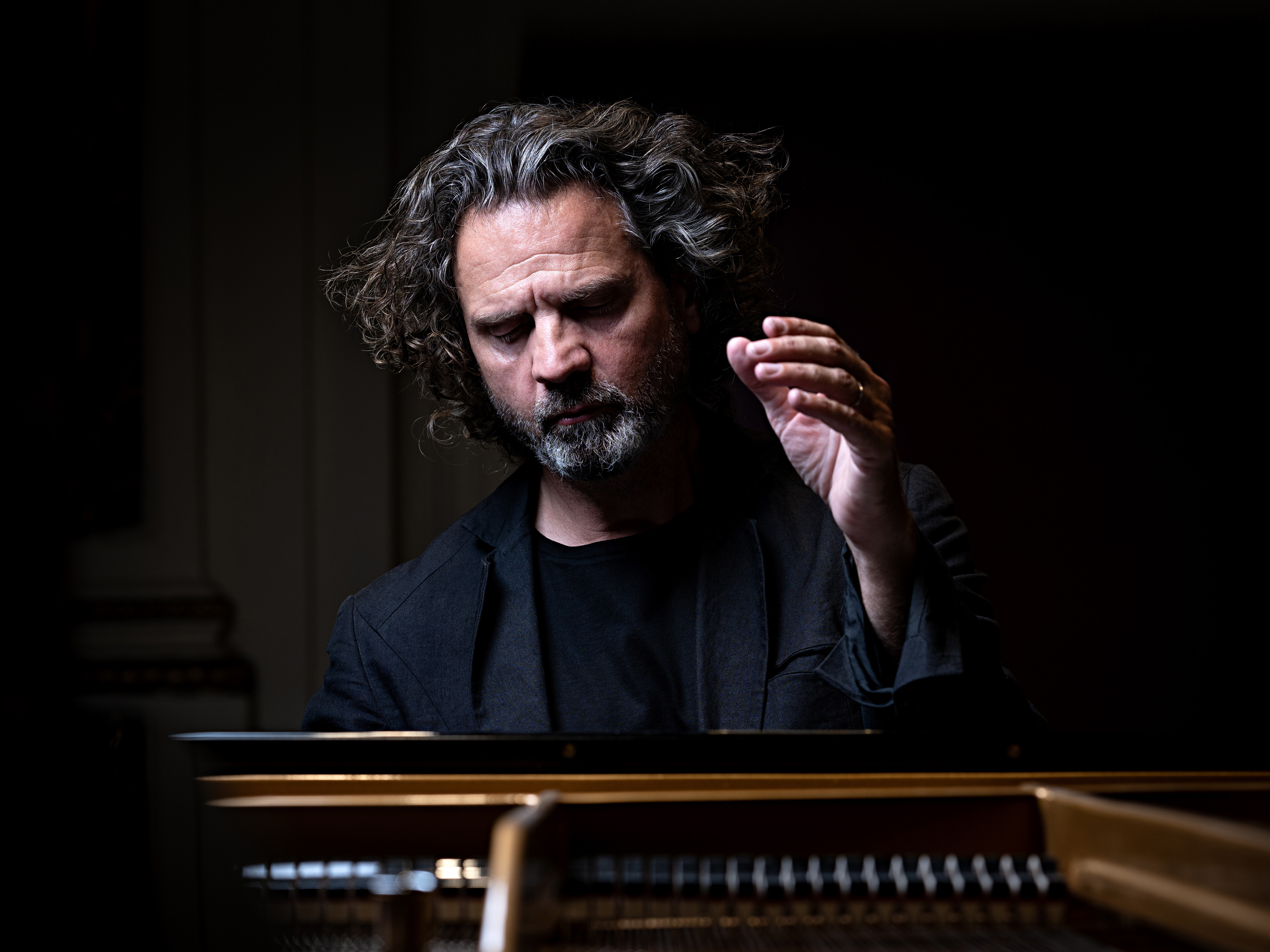 Andreas Haefliger sitting in front of a piano with one hand raised