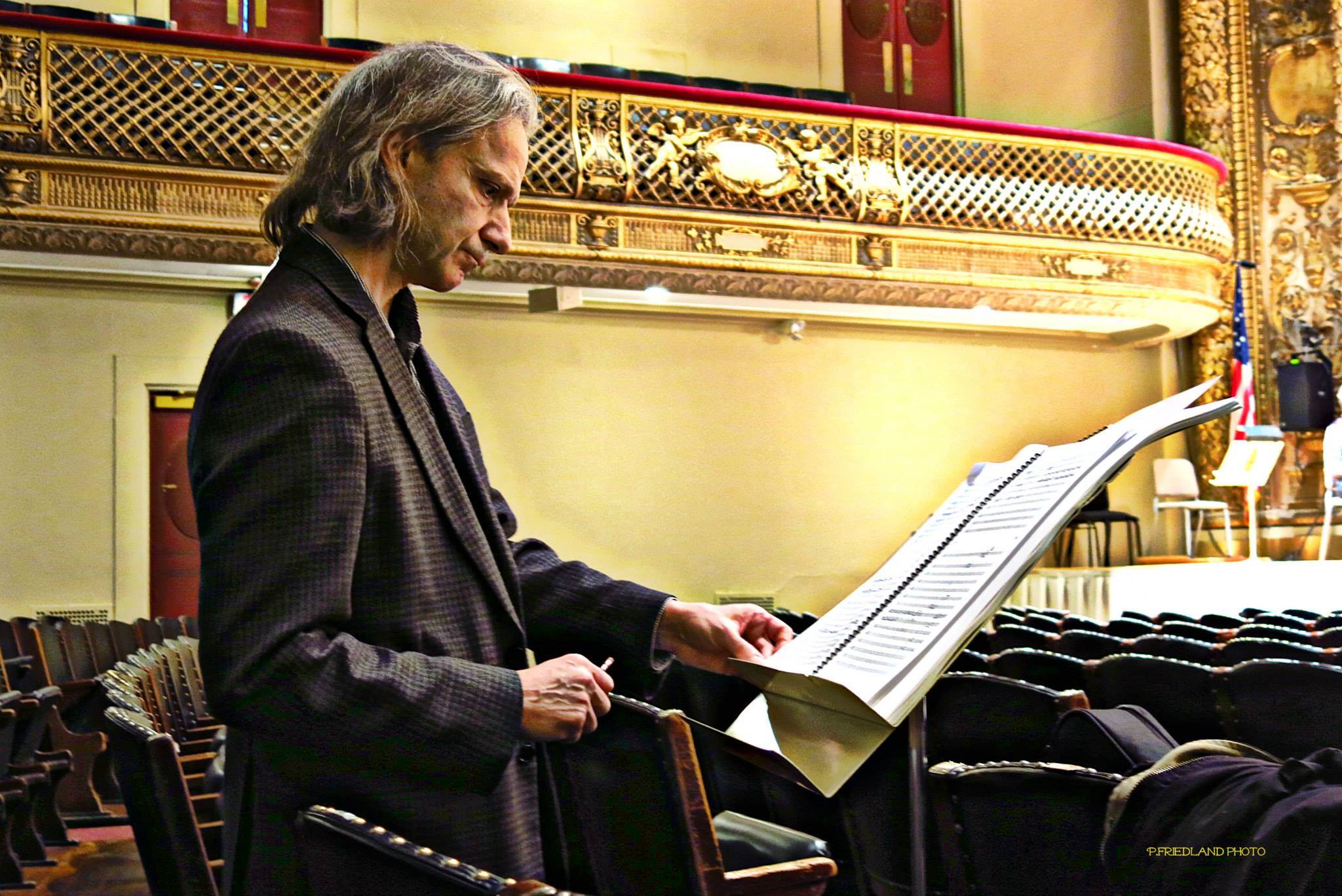 Michael Gandolfi standing in the audience of Symphony Hall looking at a music score on a music stand.