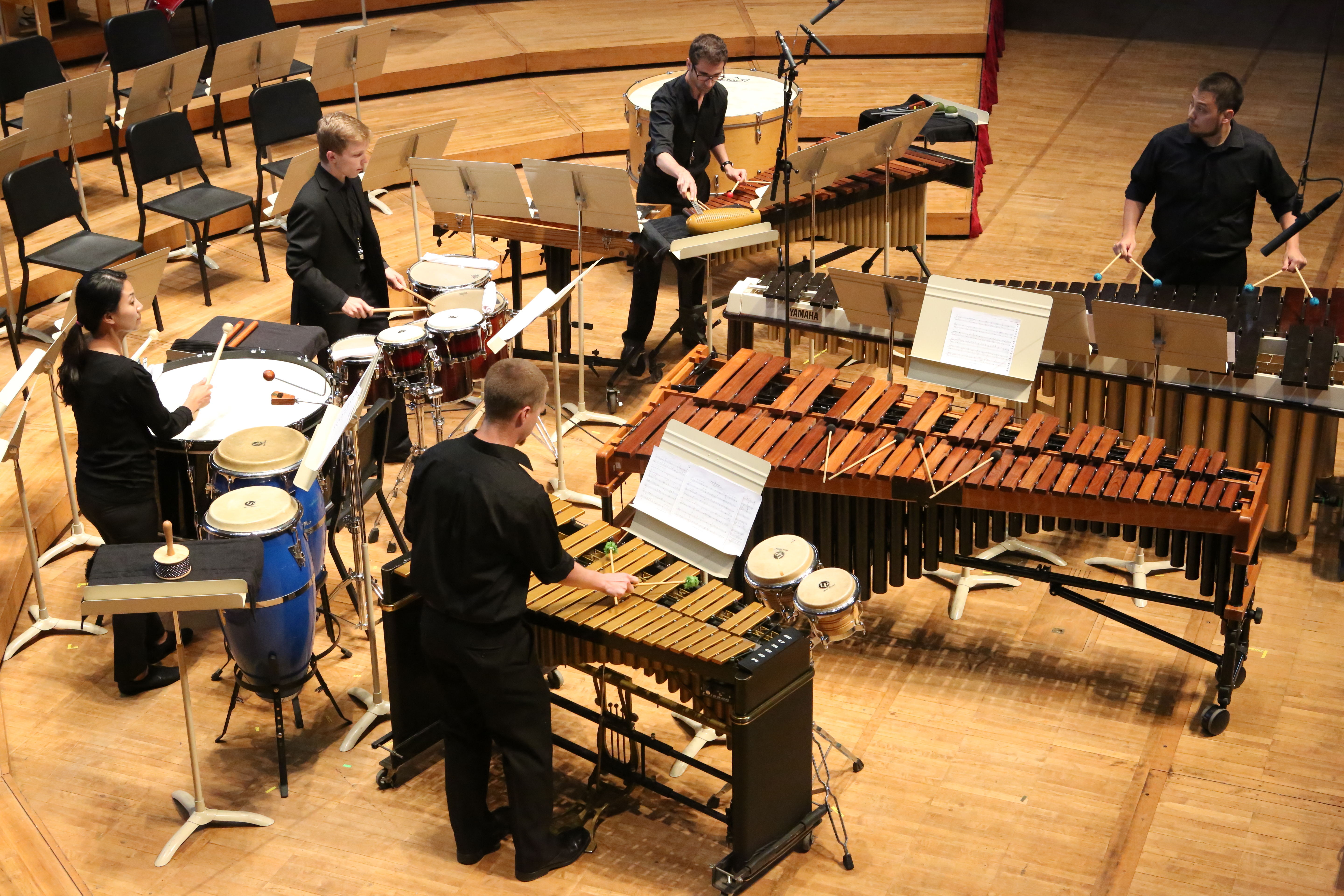 5 percussionists performing onstage, playing multiple mallet percussion instruments and drums.