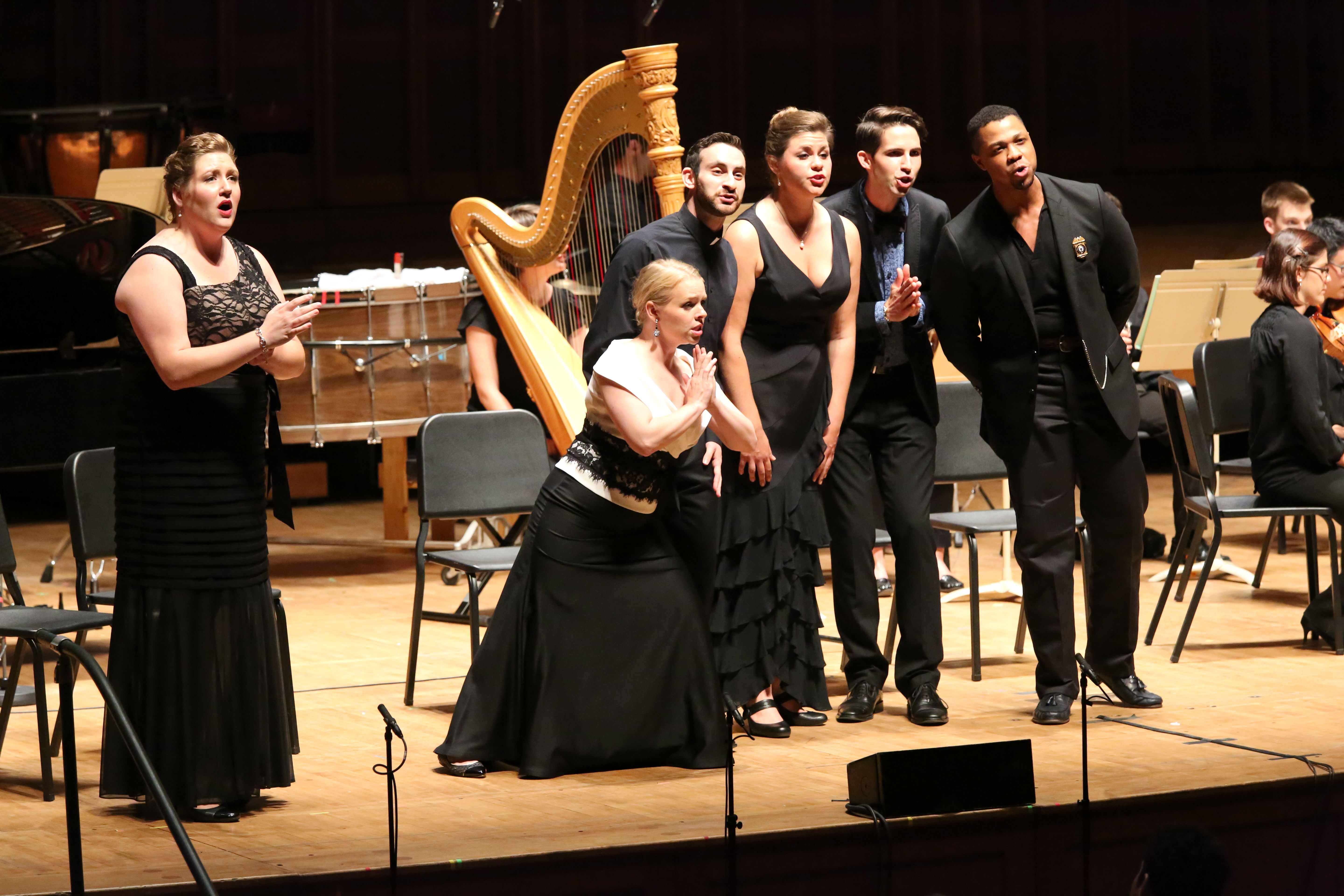 Singers perform onstage with a harp and other musicians.