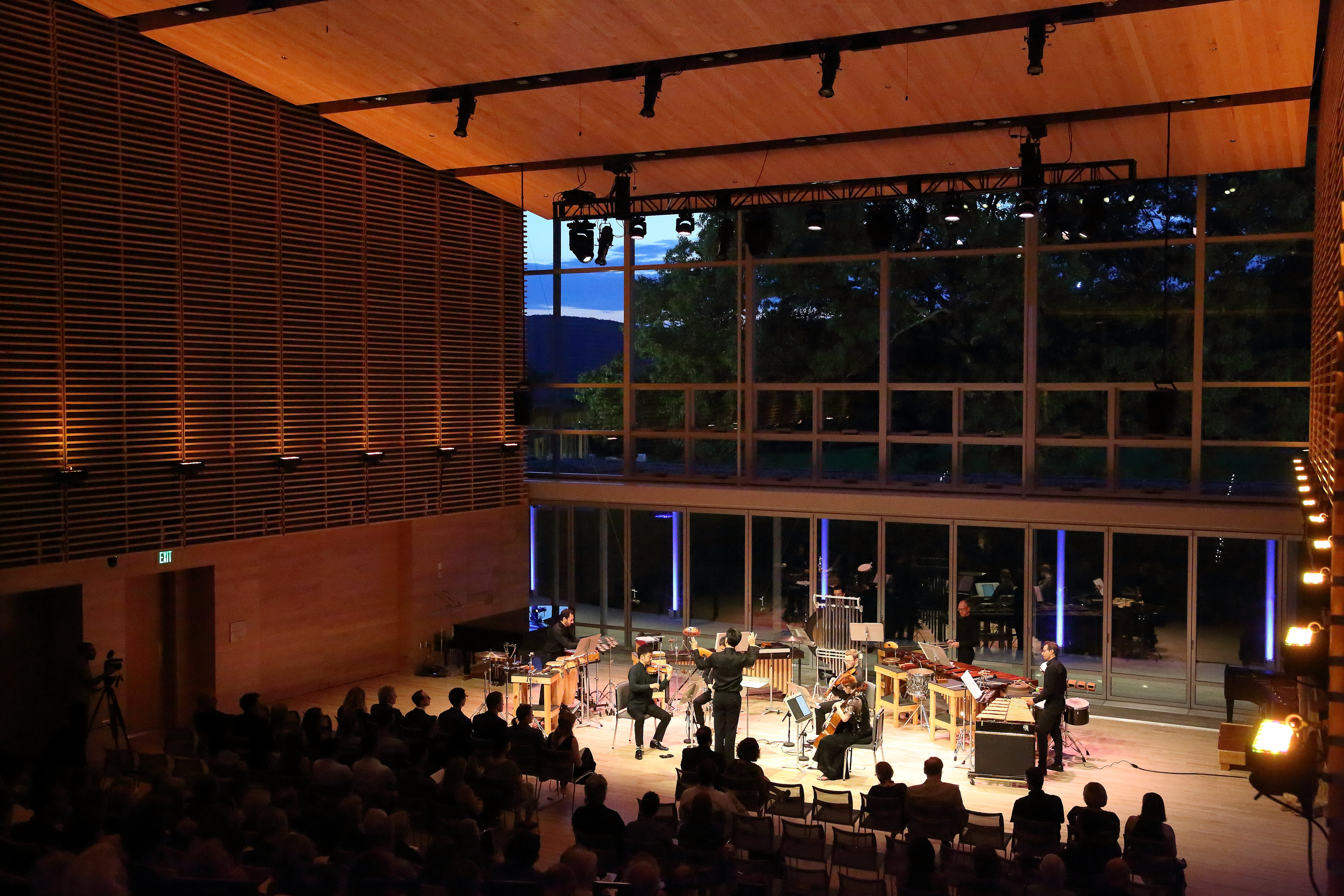A small instrumental ensemble performs in the Linde Center's Studio E, with lights on them and the rest of the room in darkness. The audience's silhouettes watch the performance