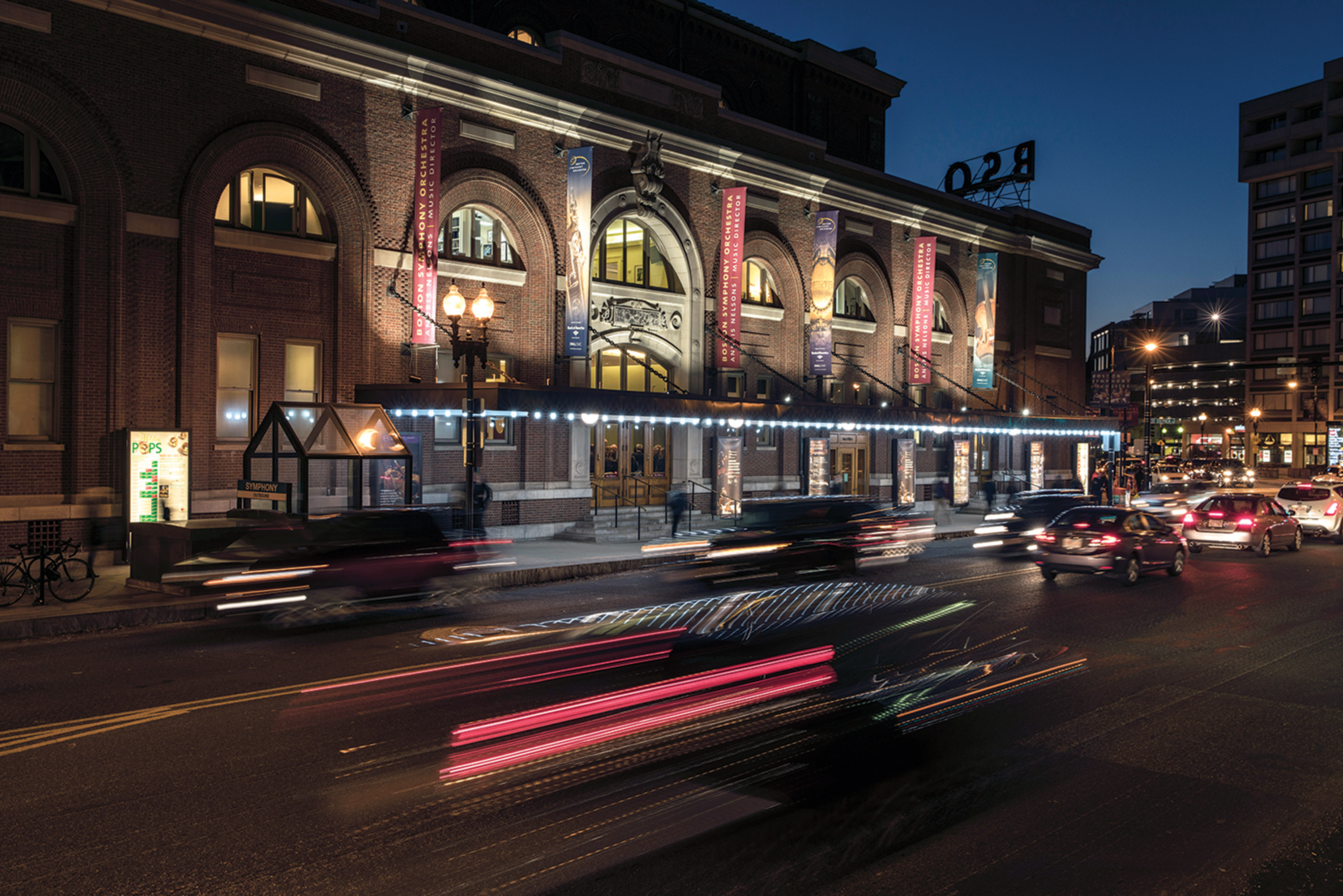 Symphony Hall exterior view of Mass Ave entrance at night with cars driving by