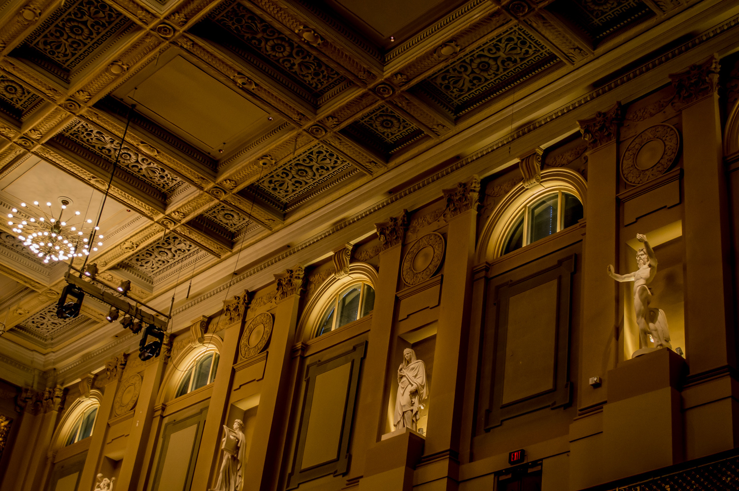 The walls and ceiling of Symphony Hall are lit in a warm light, showing their ornate molding and the statues lining the wall