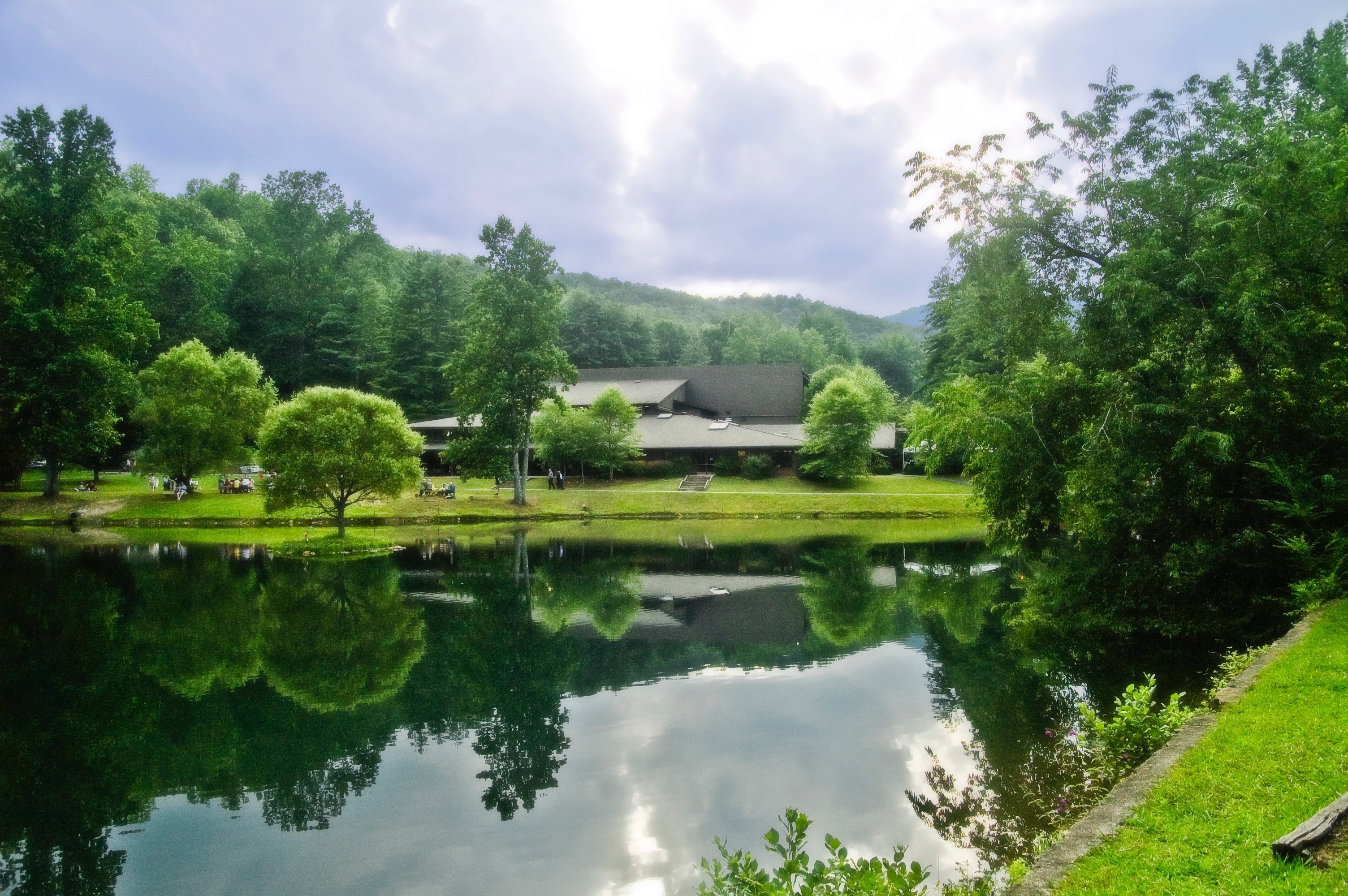 A pond reflects trees, bright green grass, and clouds at the Brevard Music Center