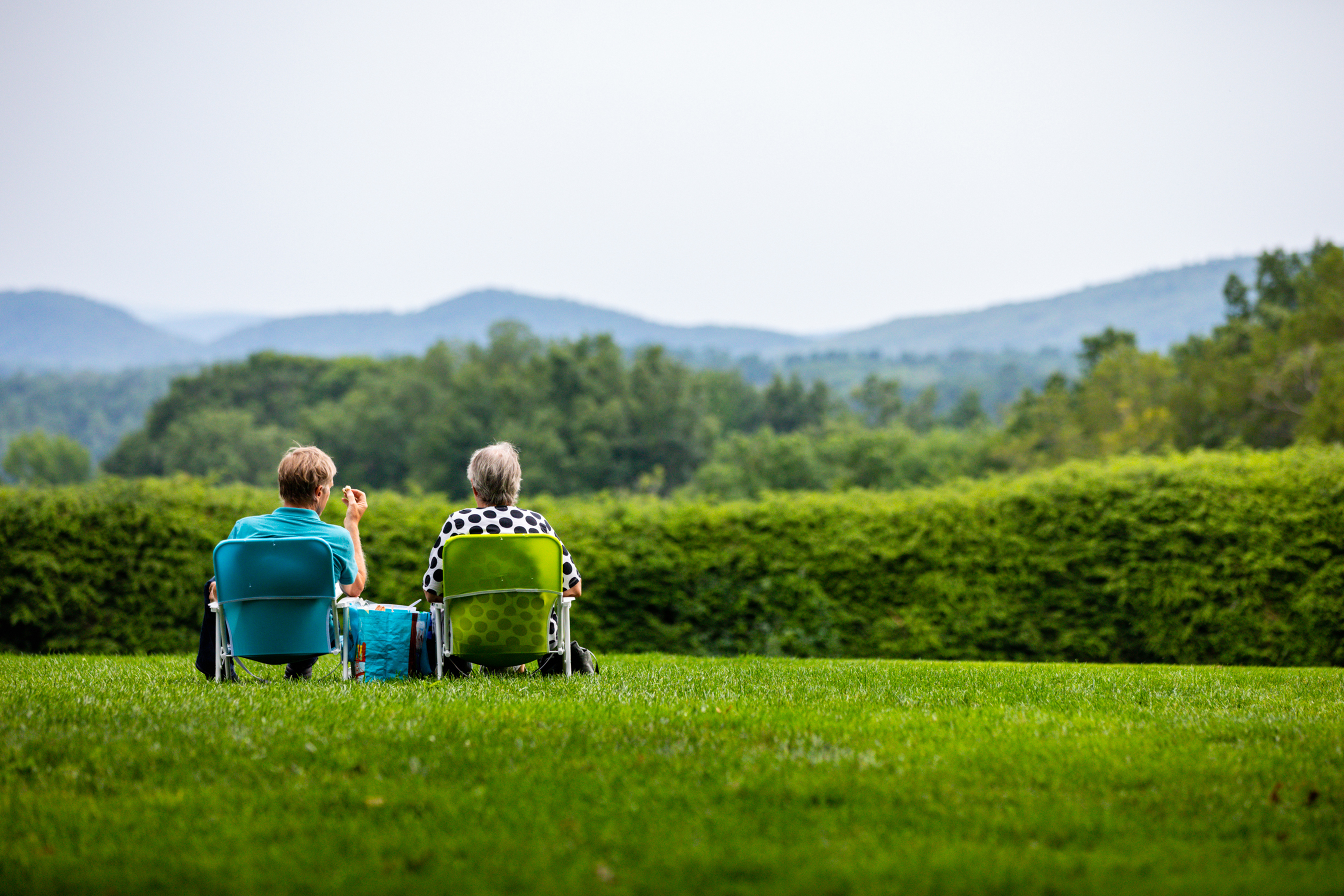 Two people sit in lawn chairs on Tanglewood lawn looking out at nature surrounding them