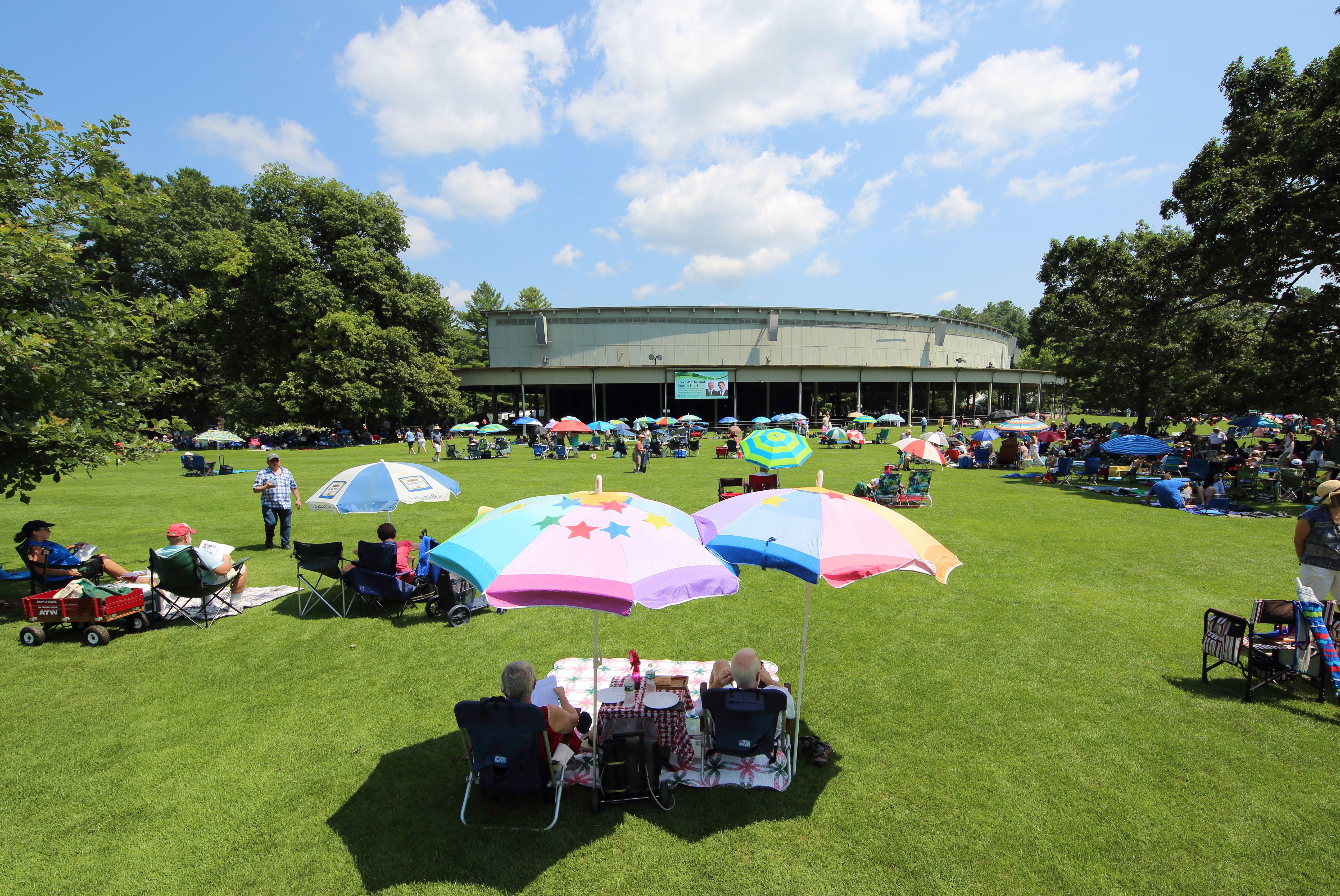 Two people sit in lawn chairs under bright umbrellas on the Tanglewood lawn