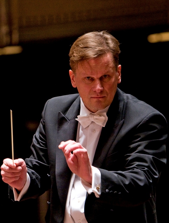 Conductor Stefan Willich wearing a black tuxedo and holding a baton