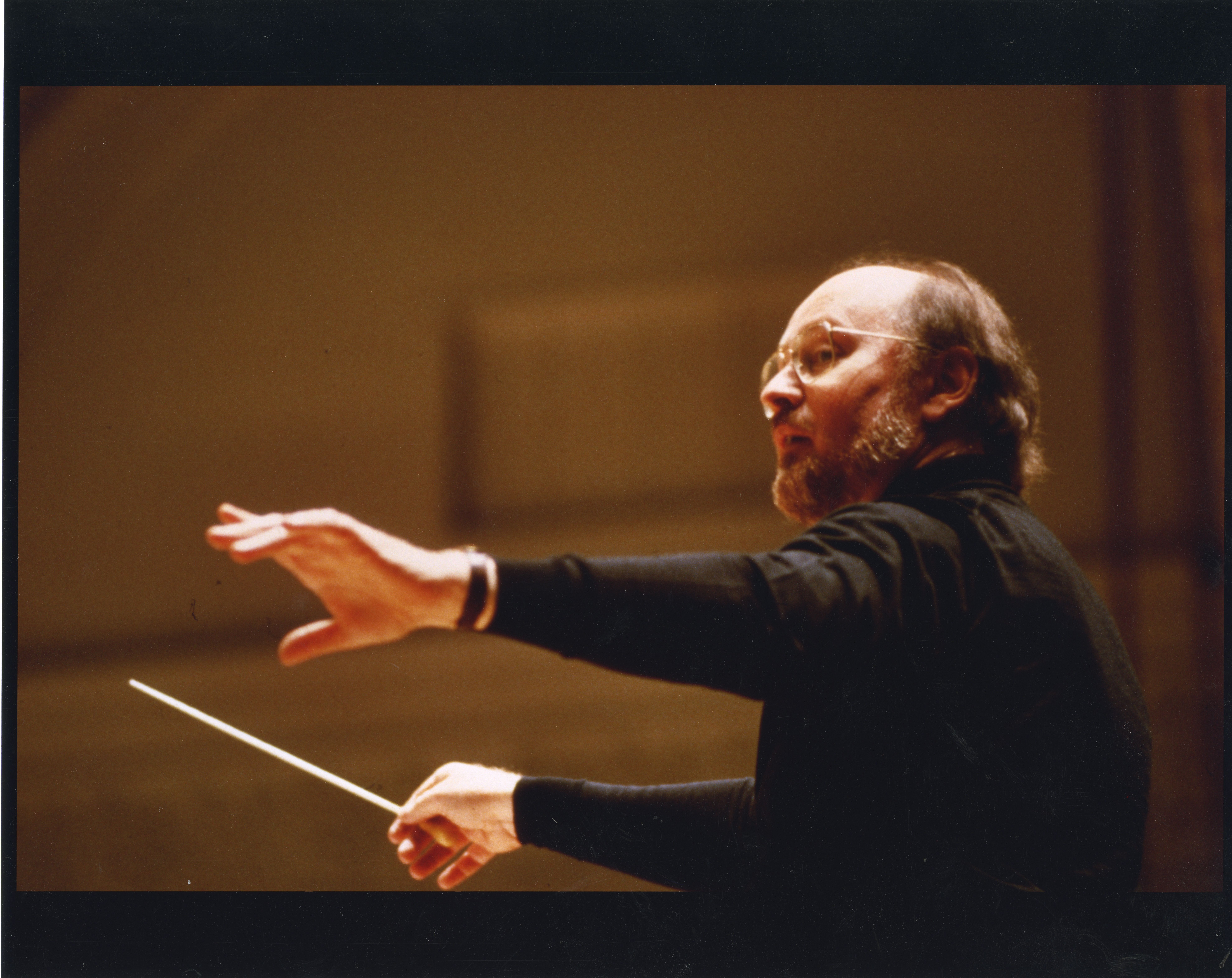 John Williams holds a baton while wearing a black turtleneck and a wristwatch