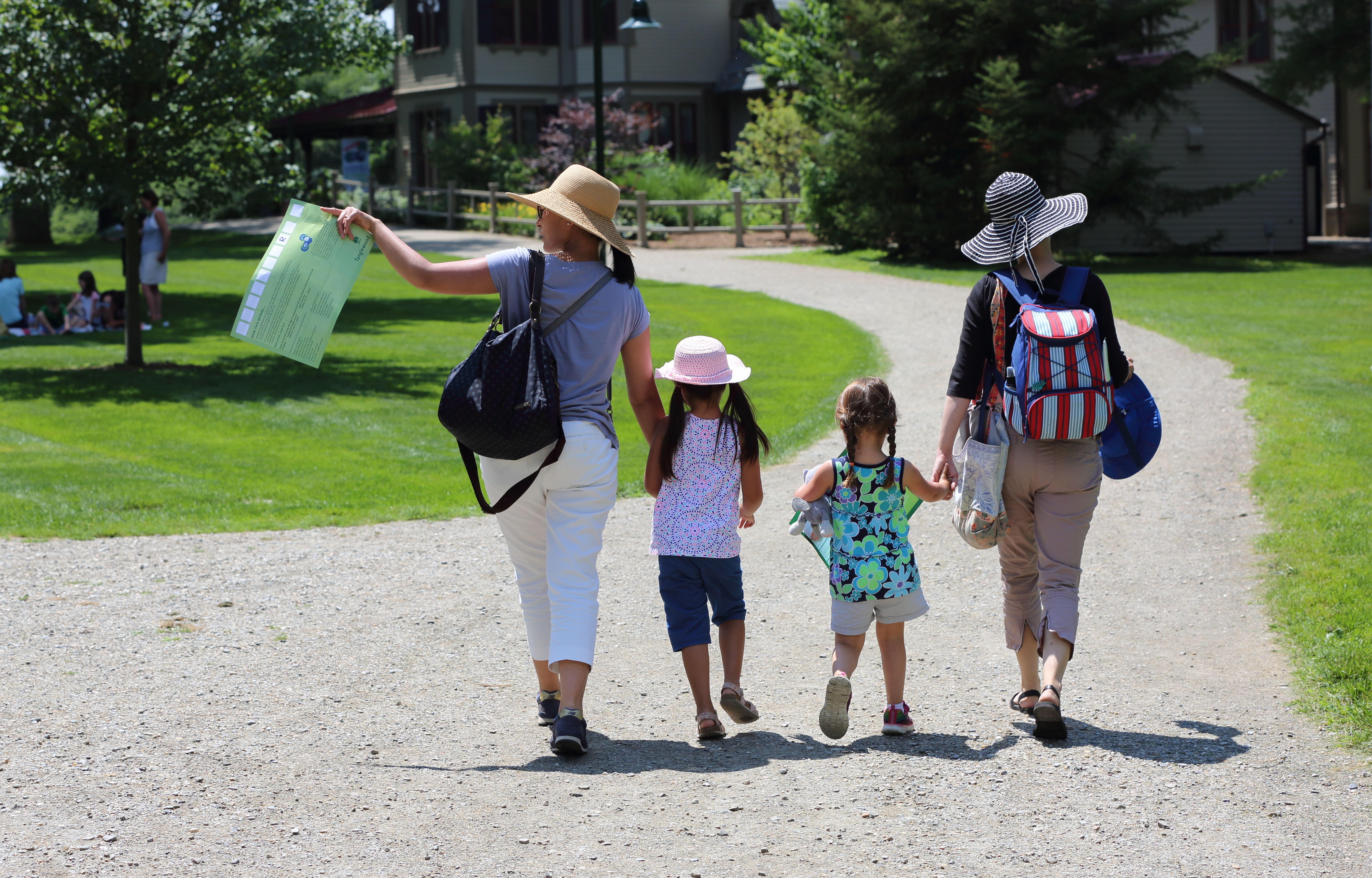 Two women holding the hands of two young girls and walking down a path at Tanglewood.